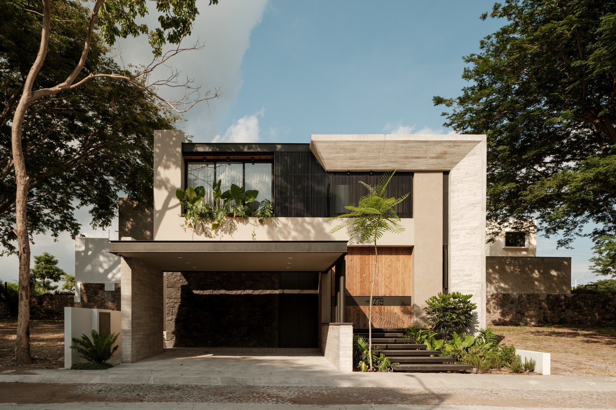 Street facade with white stucco, dark vertical slats, and timber cladding framed by mature trees
