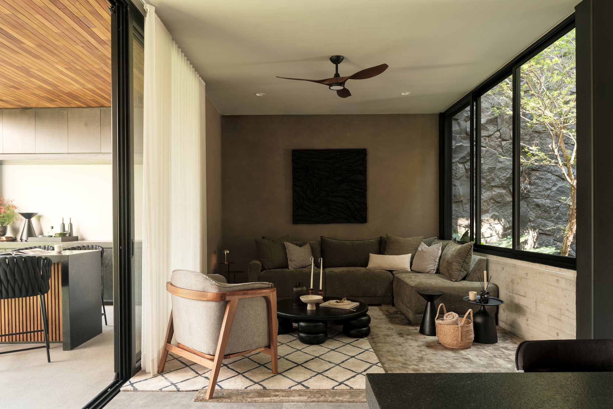 Living room opening to kitchen through black-framed glazing with sheer curtains and patterned floor tiles