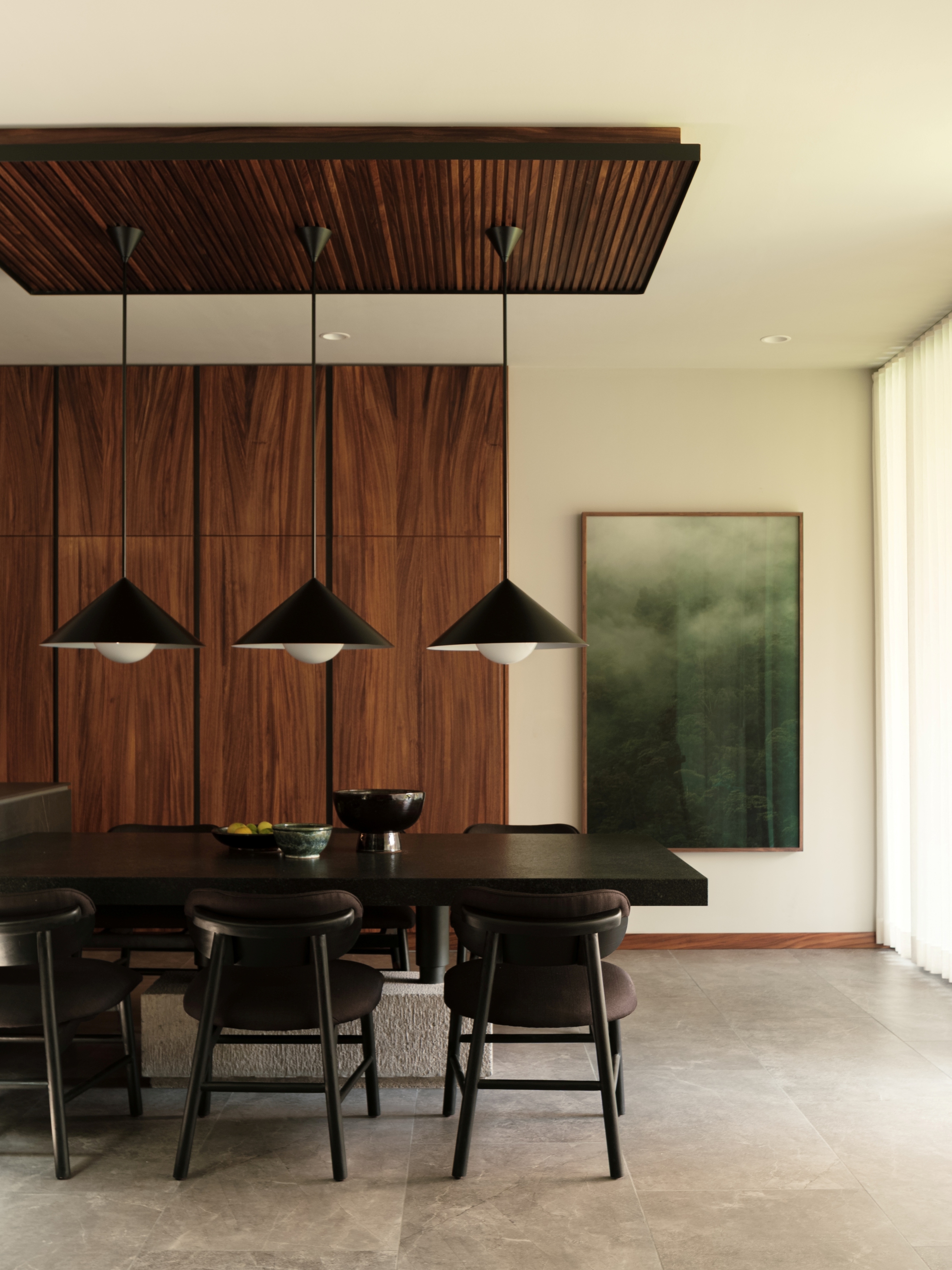 Dining area with three black pendant lights hanging over a dark table against wood-paneled walls