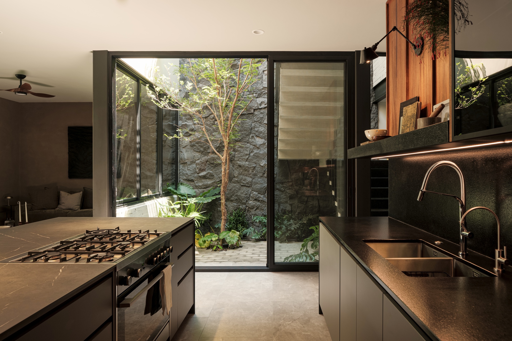 Kitchen prep counter facing a planted courtyard with stone walls through open sliding glass doors