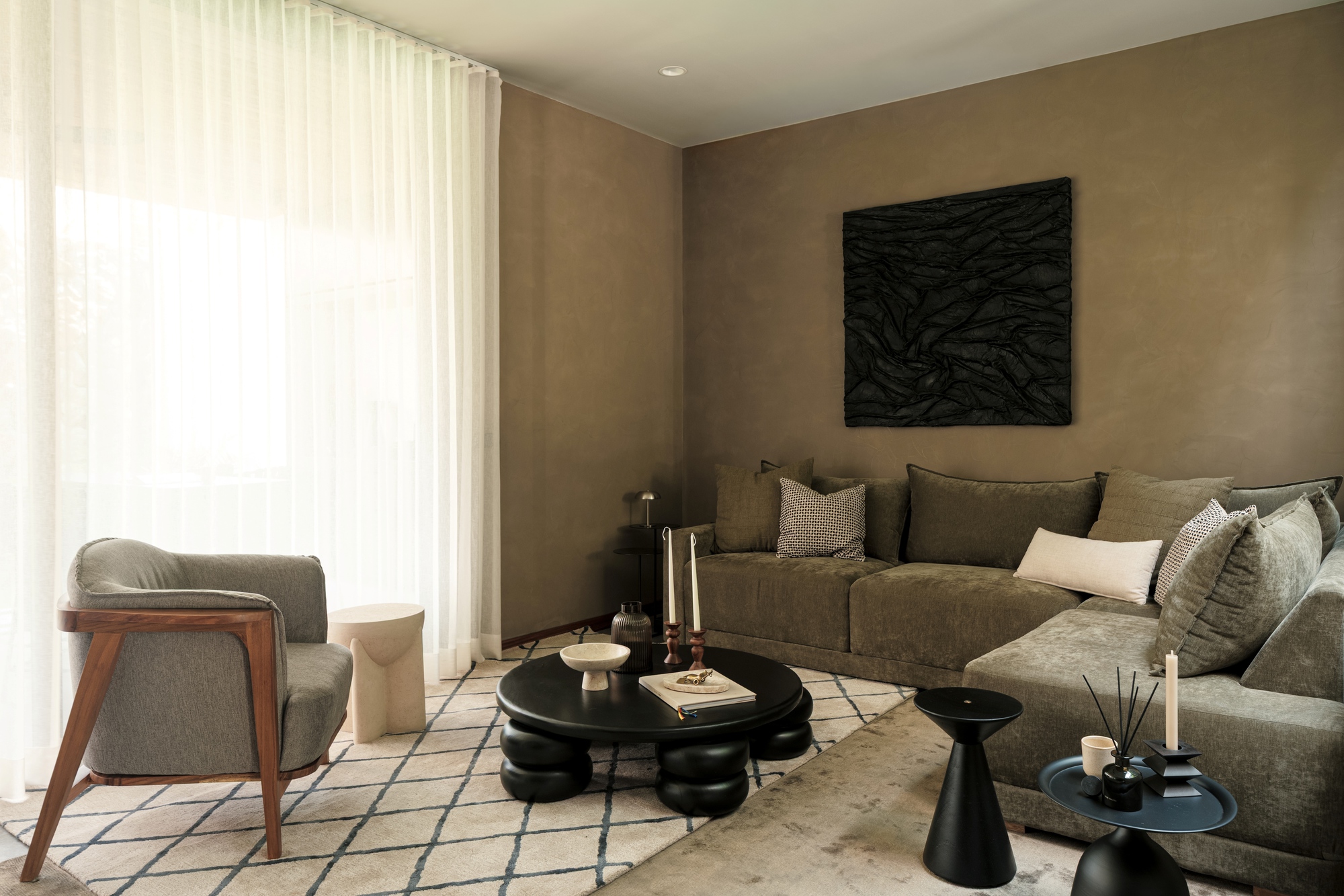 Living room with tan plaster walls, sheer curtains filtering daylight, and a sectional sofa facing black tables