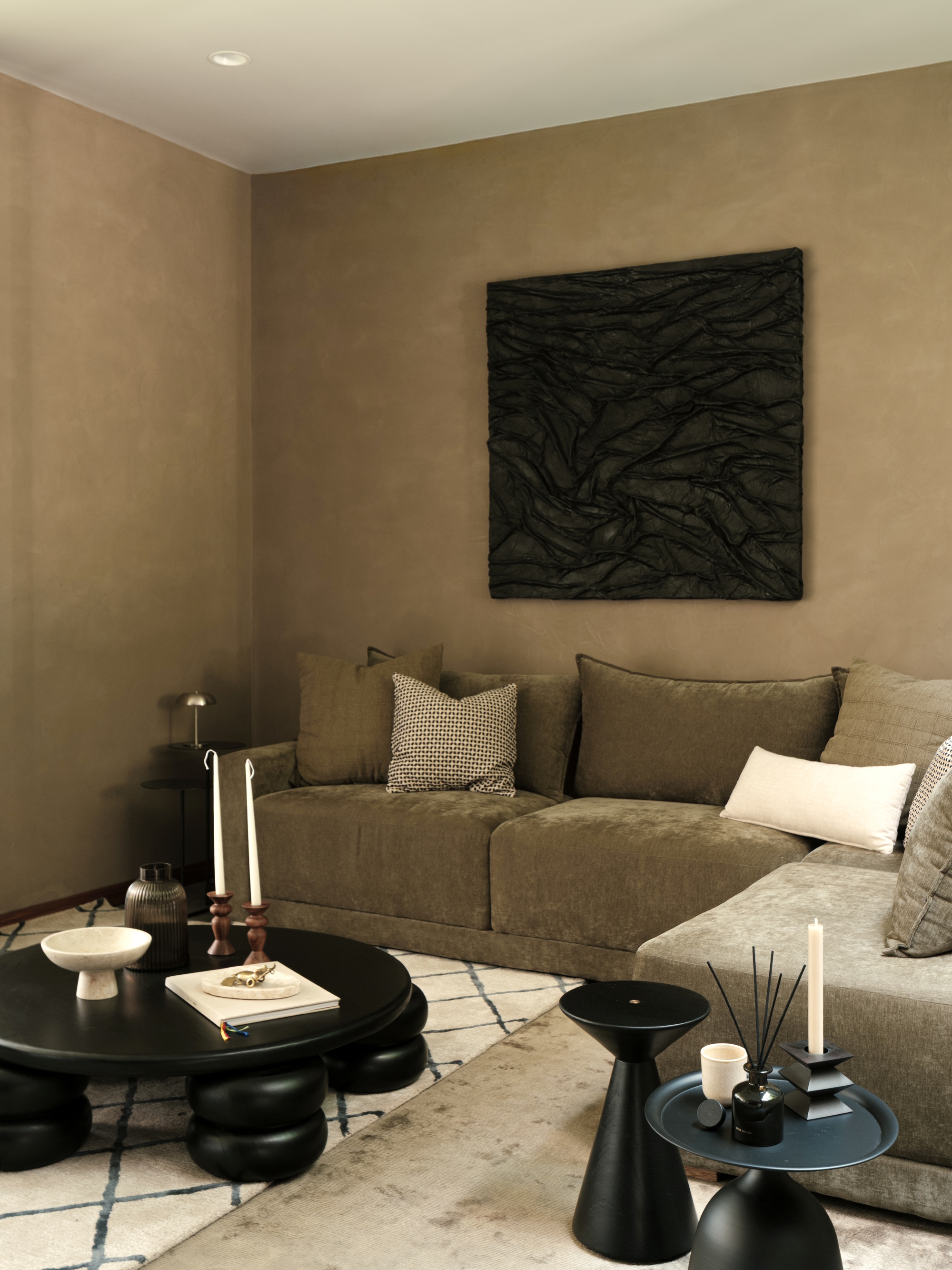 Corner seating arrangement beneath a dark textured artwork with black sculptural side tables and candles