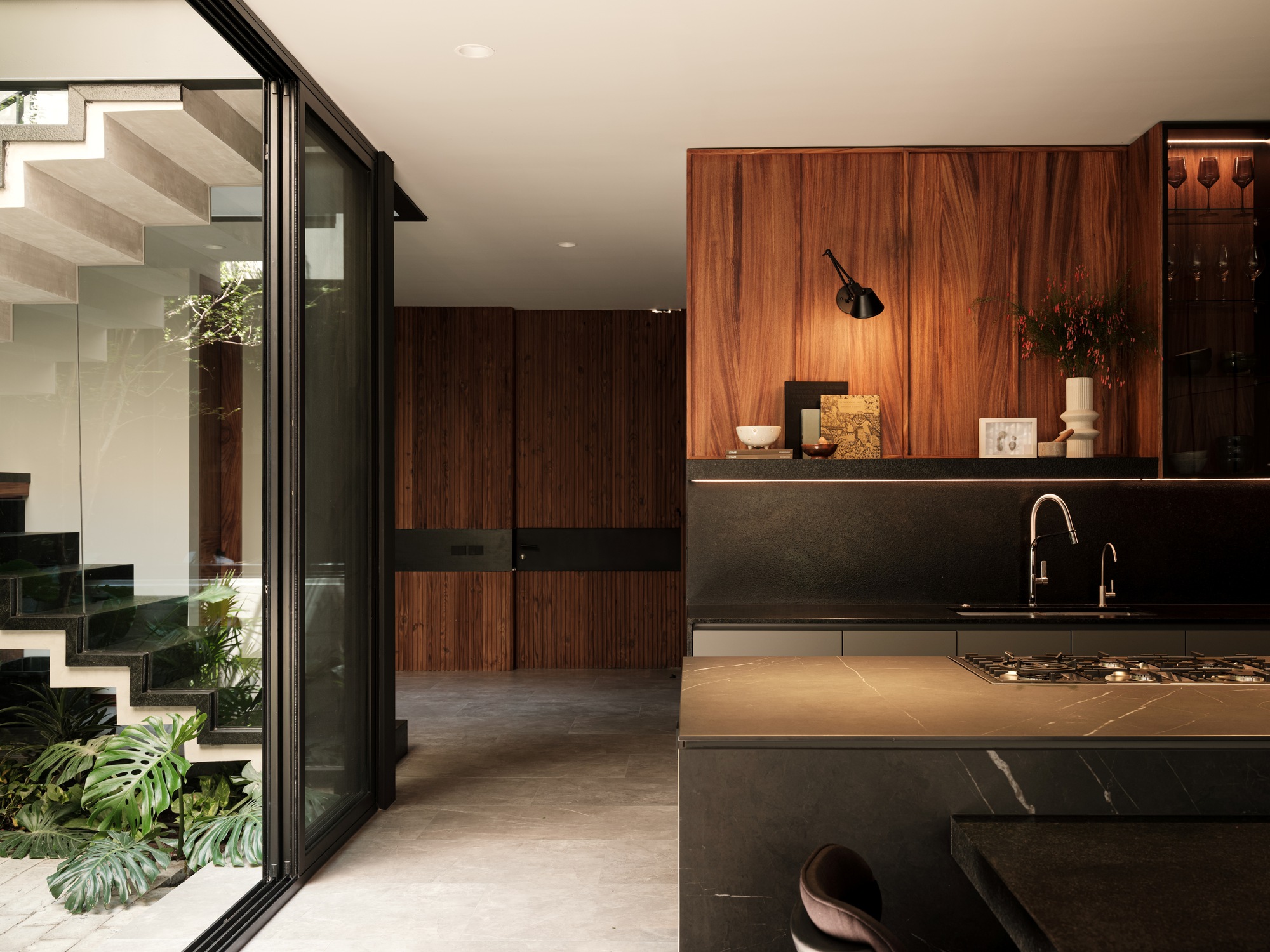 View from courtyard through glazed doors toward kitchen counter with marble surface and timber storage wall