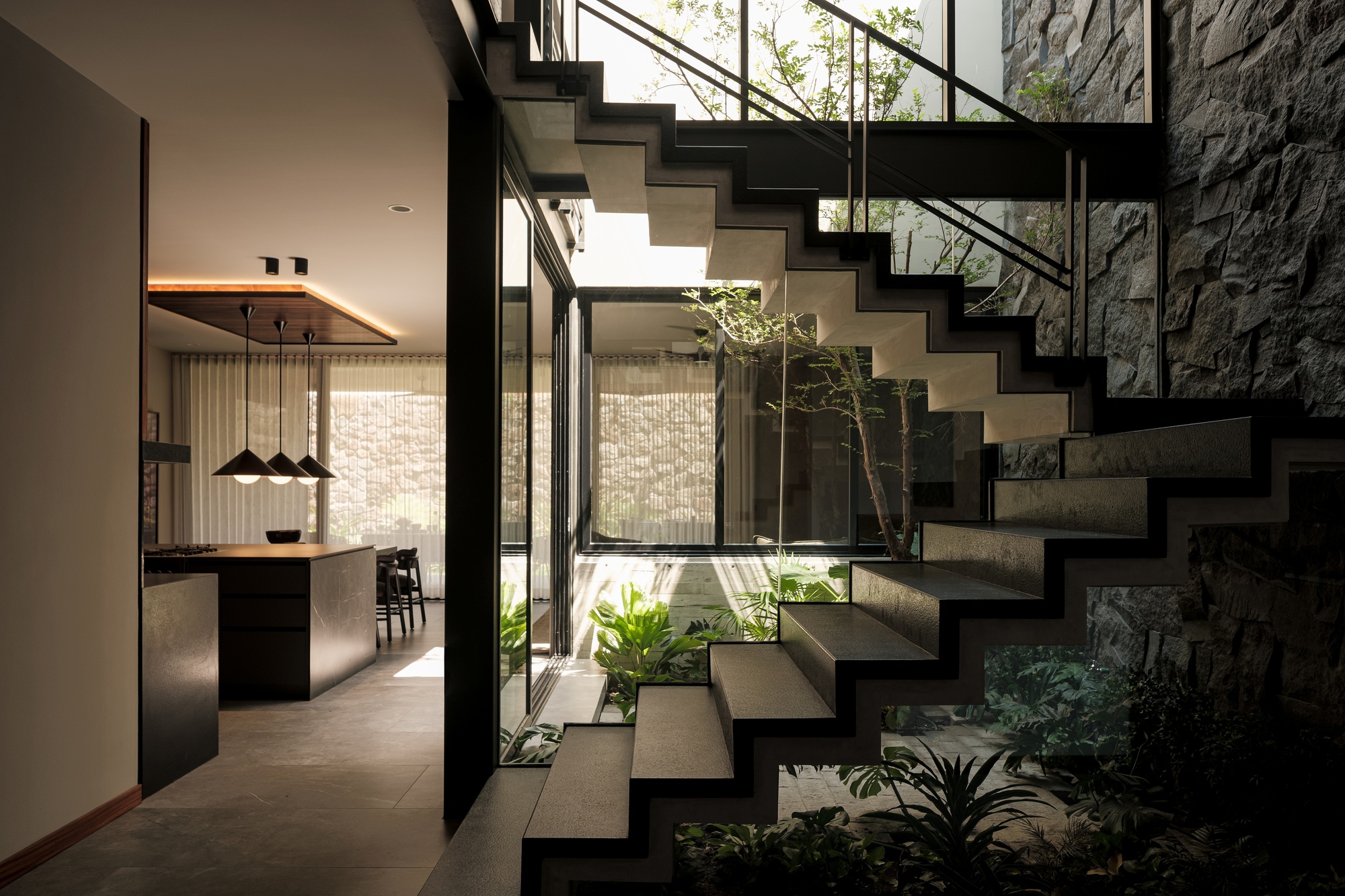 Floating concrete staircase beside a planted courtyard with ferns and stone wall cladding