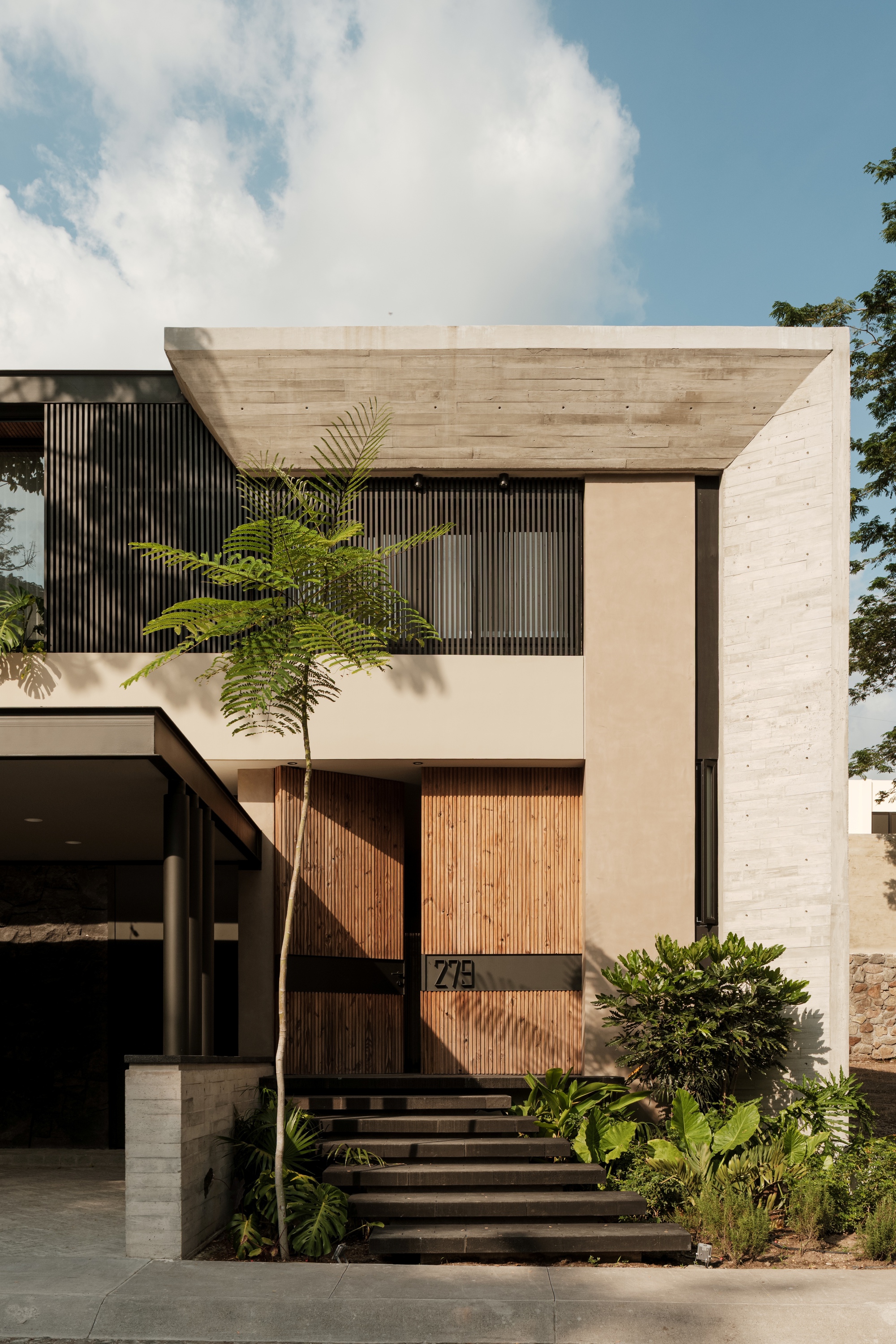 Entry facade showing board-formed concrete frame, vertical wood screens, and timber entry steps