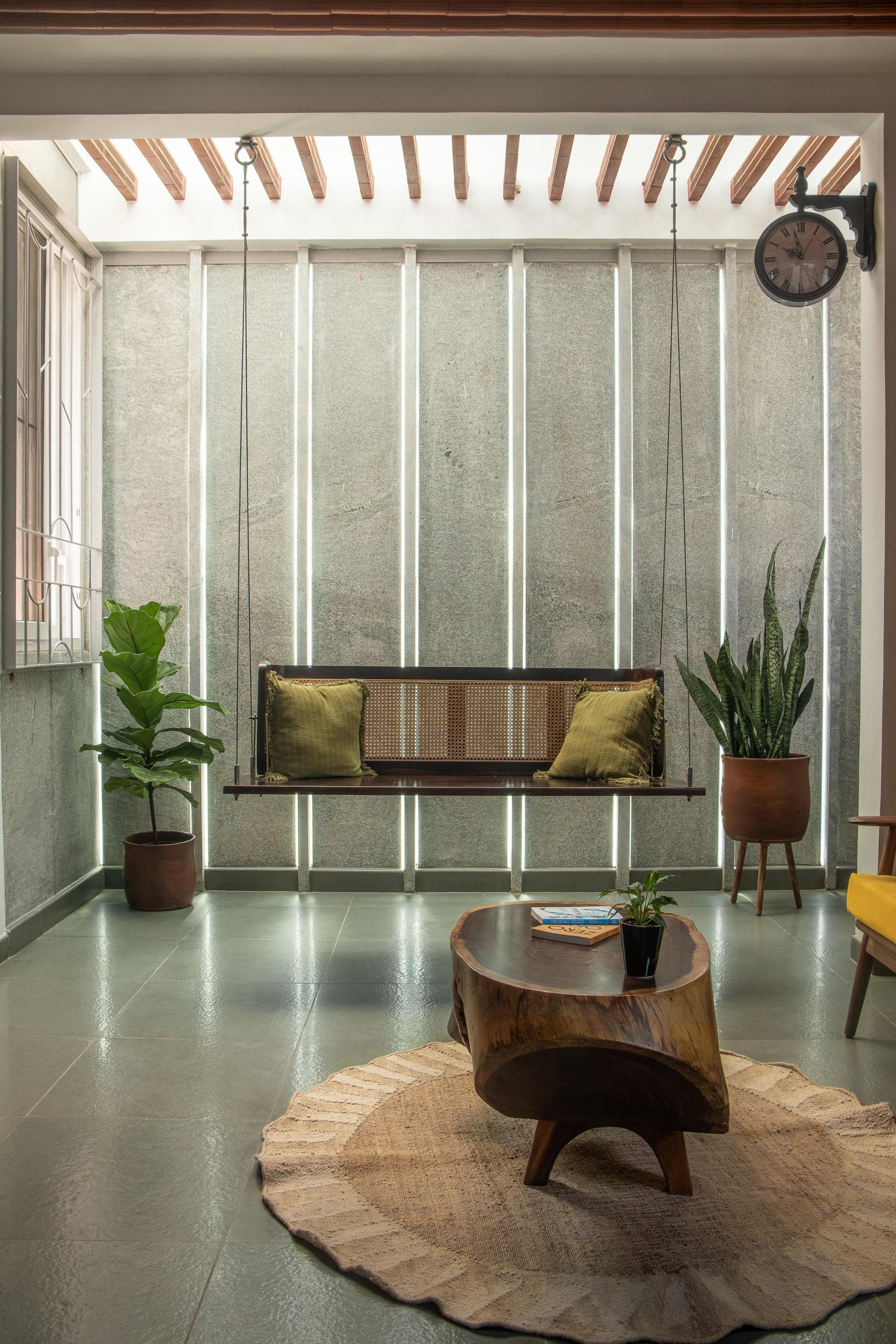 Living room with vertical backlit panels in the concrete wall and a suspended cane swing seat