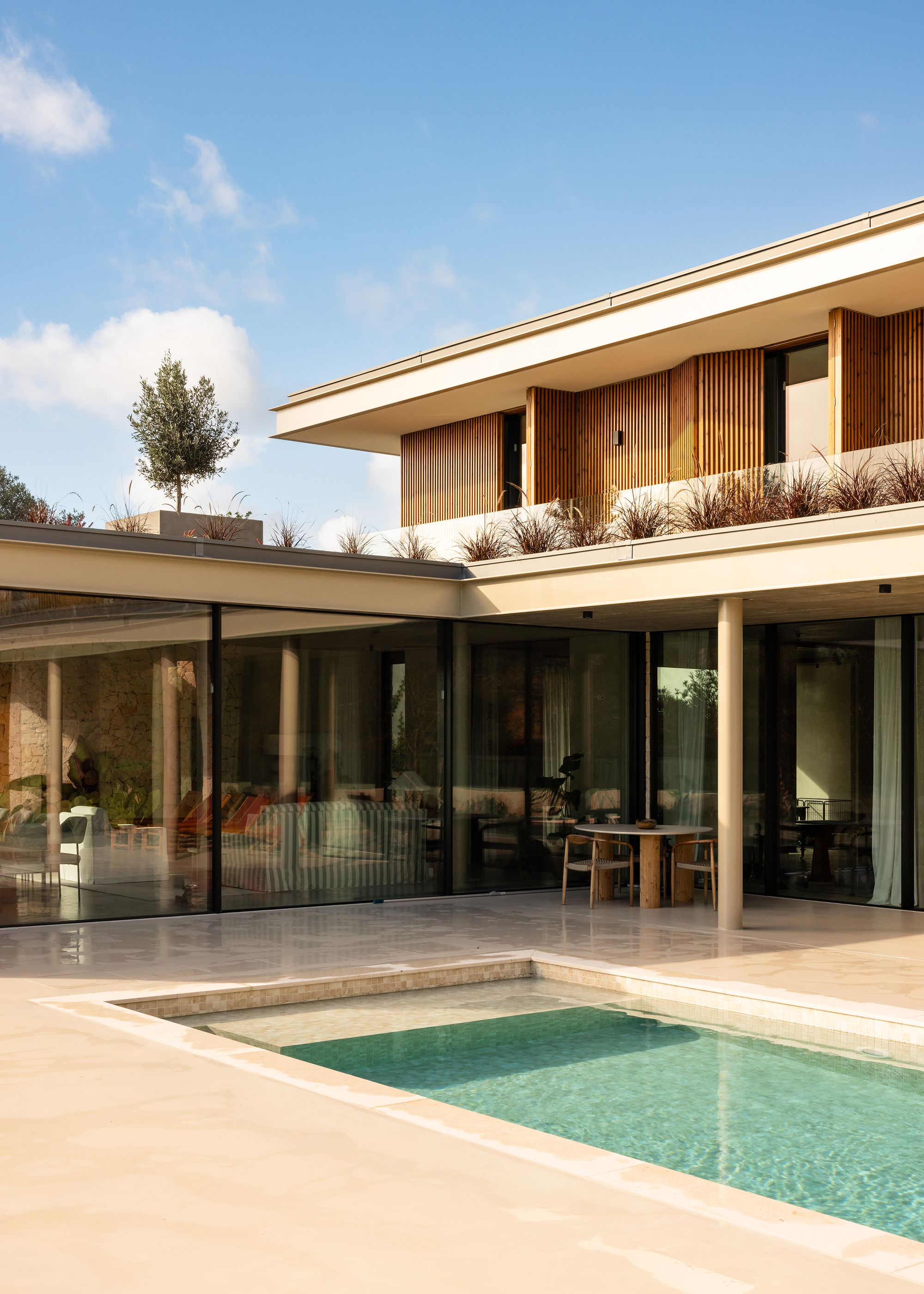 Terrace with limestone pool surround adjacent to glazed living spaces and planted upper-level balcony with grasses
