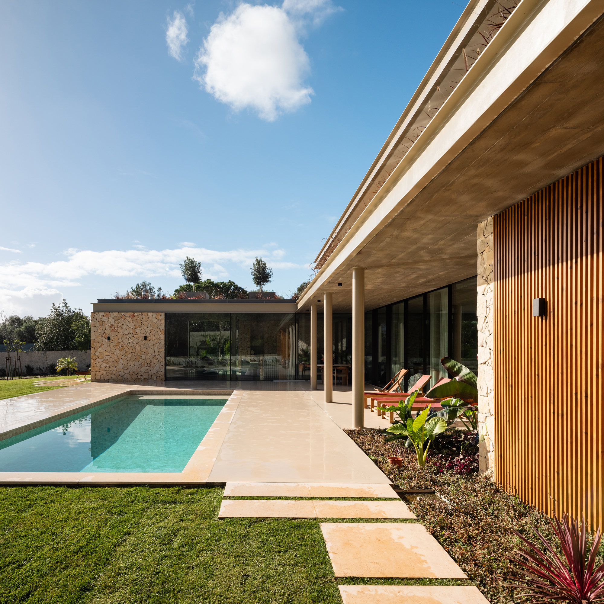 Covered terrace with timber soffit and vertical wood screening beside the pool and lawn stepping stones