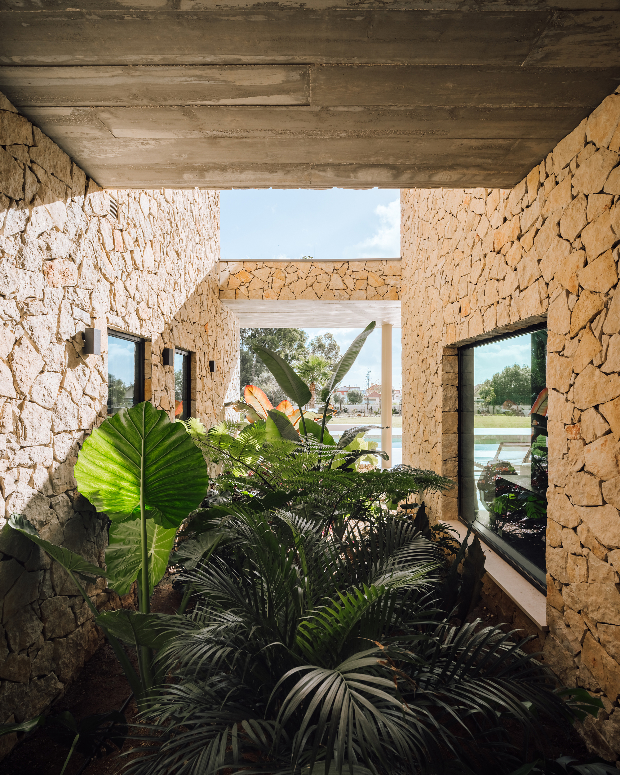 Interior courtyard with rough-cut stone walls, board-formed concrete ceiling and lush tropical plantings below