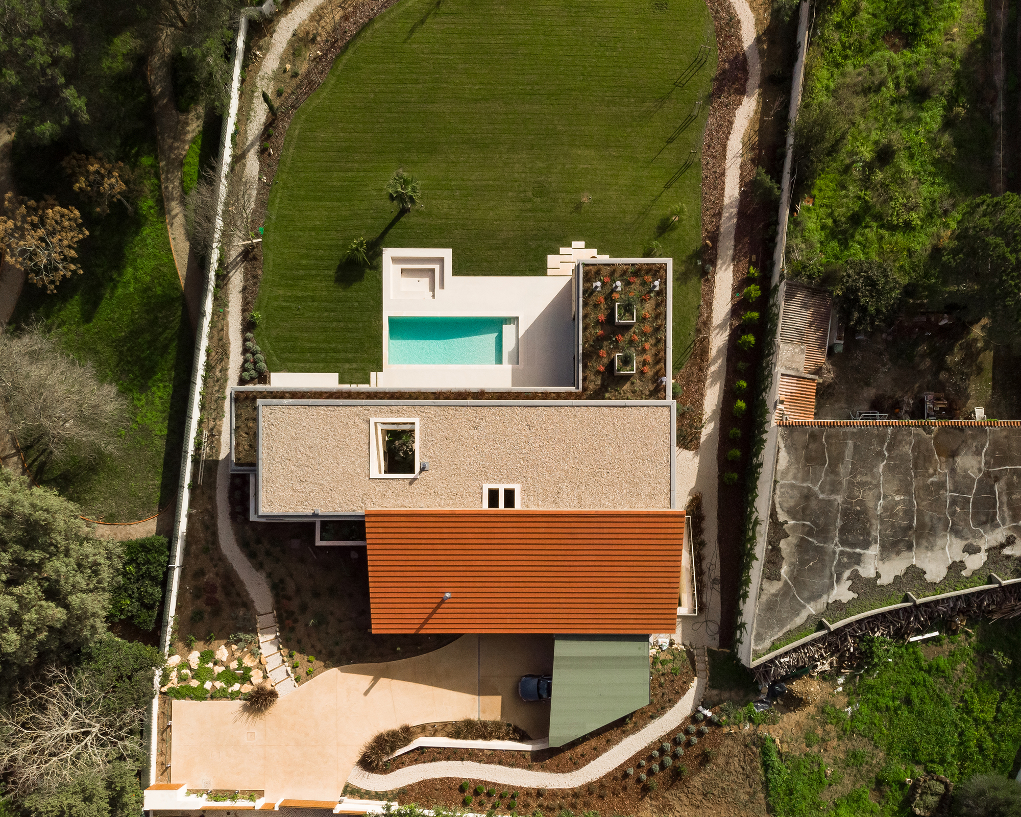Aerial view of the residence showing white and timber volumes with pool and green roof terrace