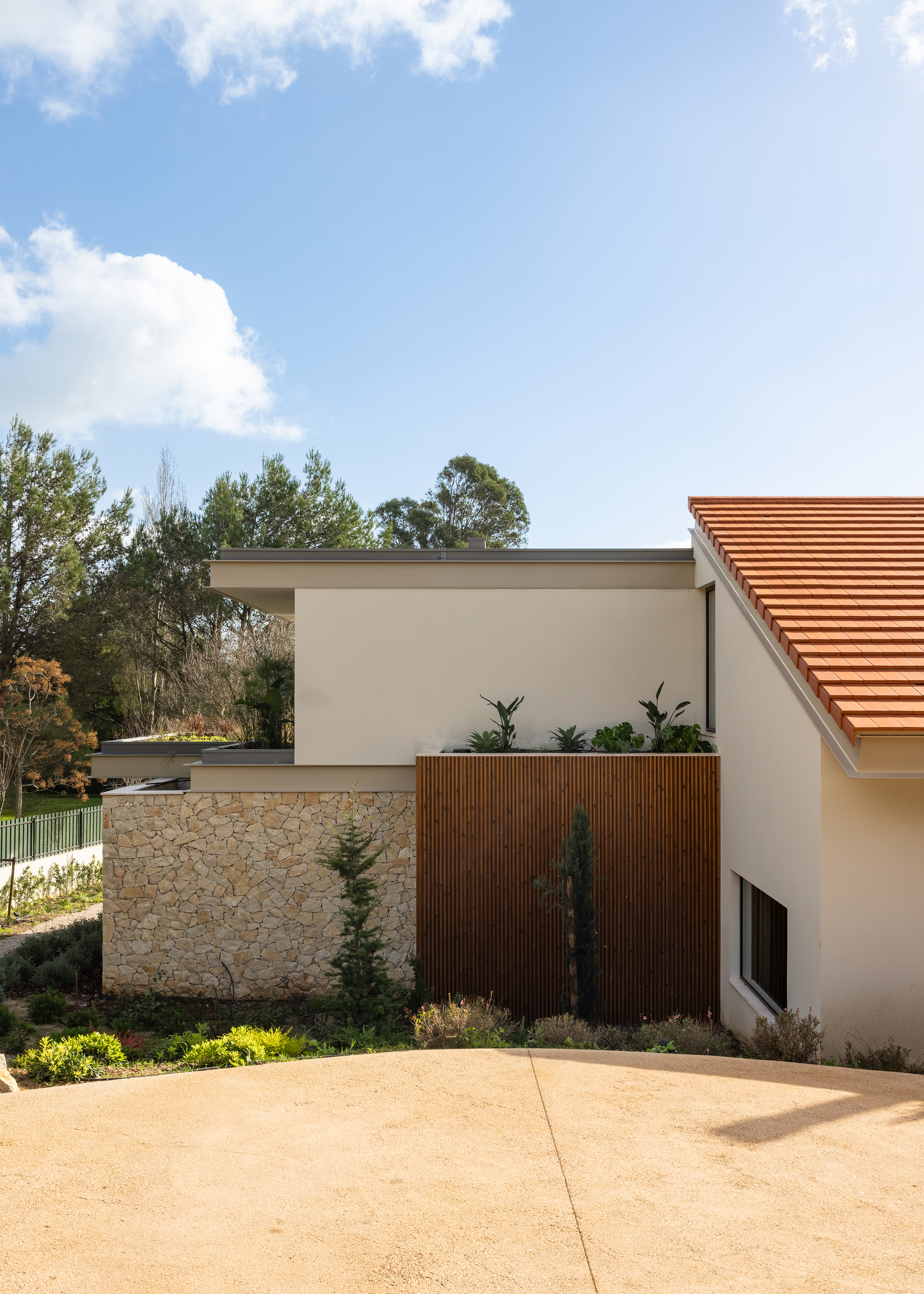 Entrance courtyard showing the layered facade with stone wall, timber cladding, and white stucco volumes