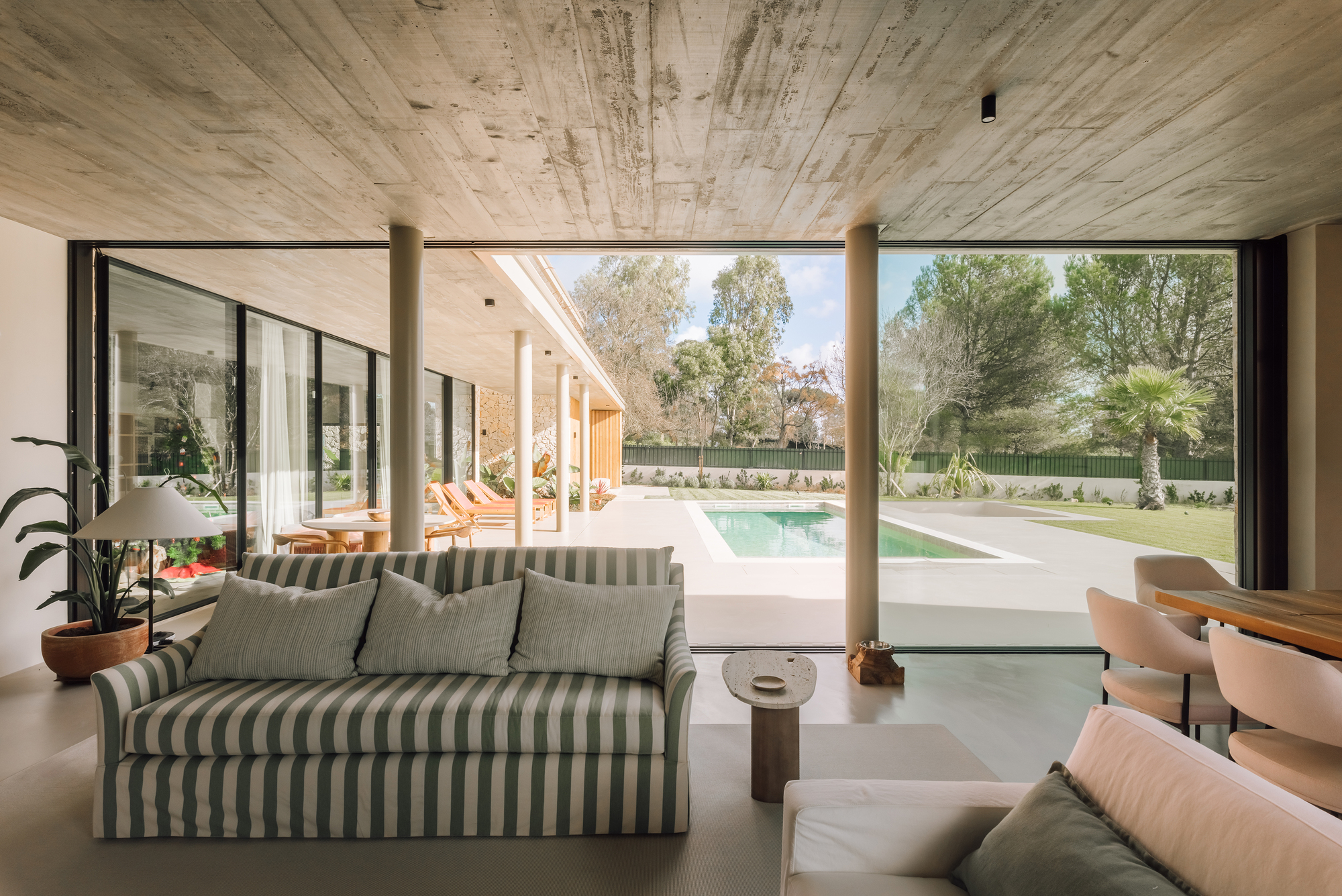 Living room with floor-to-ceiling glazing opening to pool terrace beneath board-formed concrete ceiling