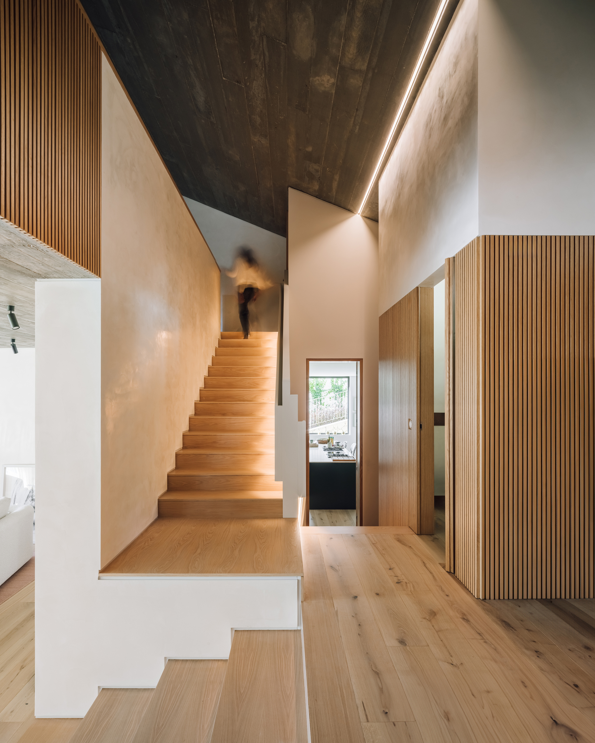 Timber staircase rising through a double-height hall with a person ascending the treads
