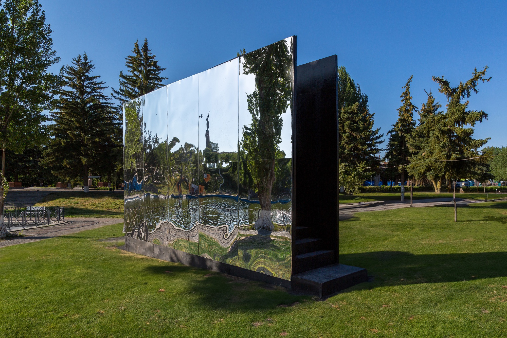 Polished metal panel with black reverse side standing in park framed by evergreen trees