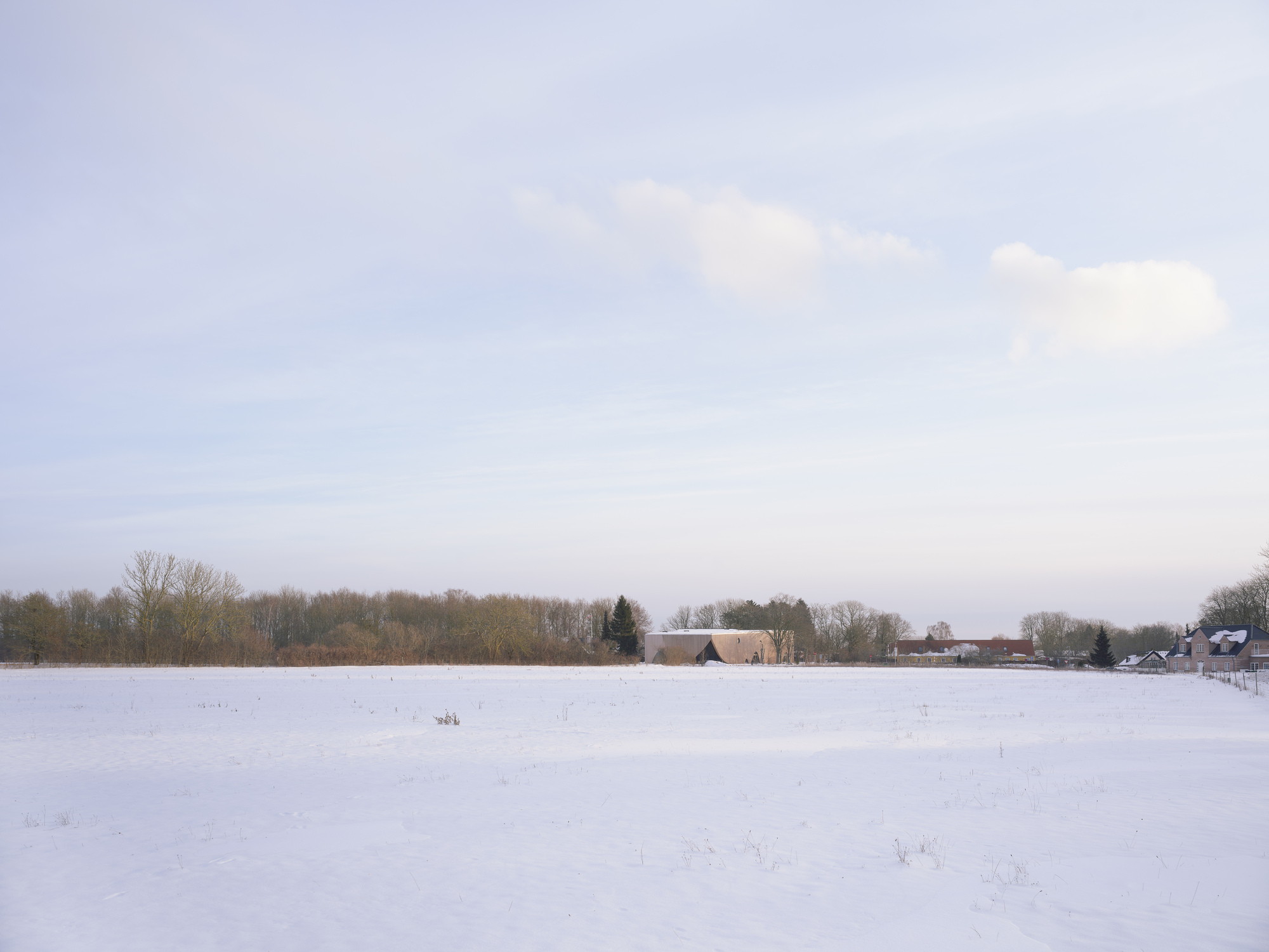 Distant view of the structure across an expansive snowfield with a tree line on the horizon