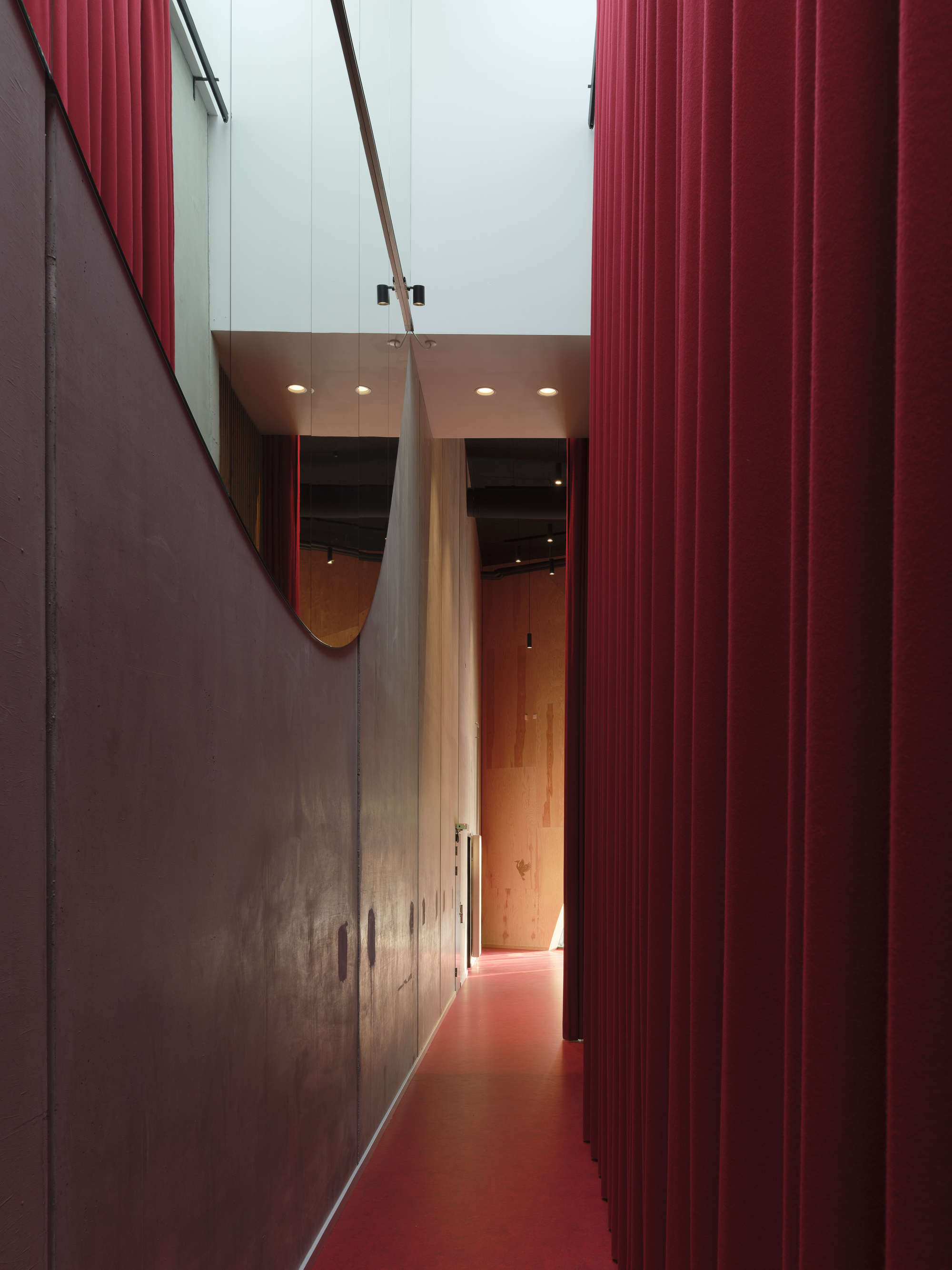 Narrow corridor with red floor and corrugated wall panels leading to a mirrored archway above
