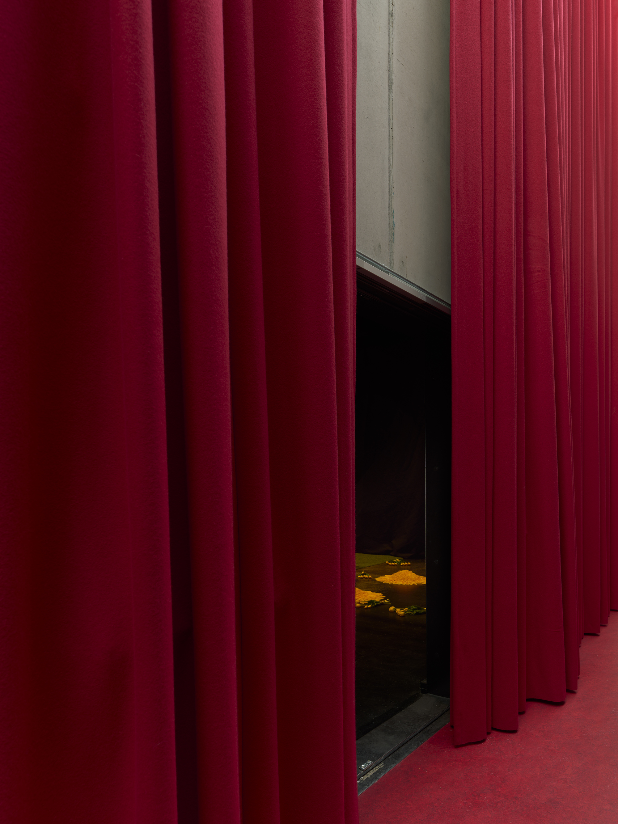 Deep red fabric curtains parted to reveal a dark theater space with painted floor visible beyond