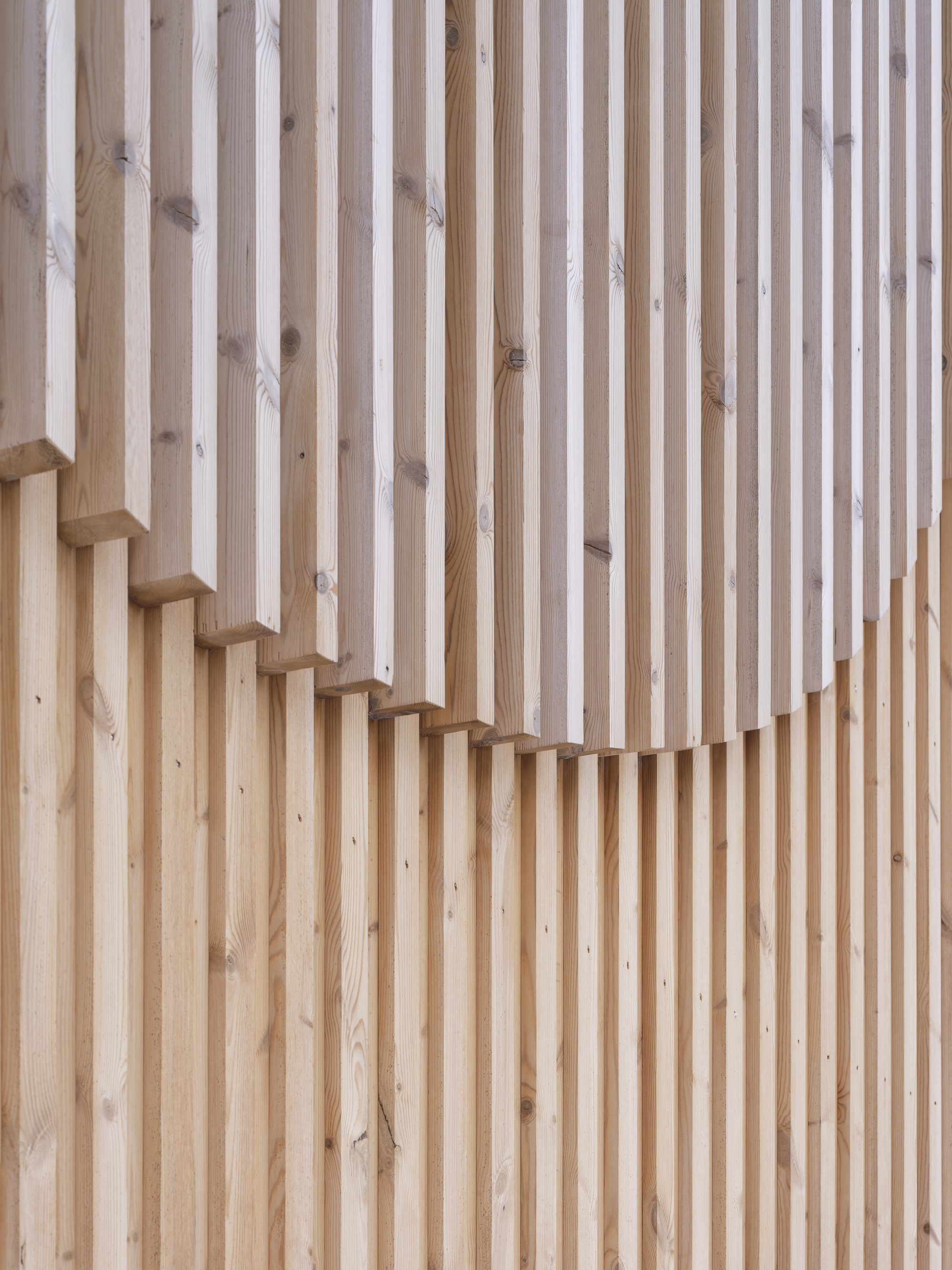 Vertical timber slat wall with a cantilevered wooden staircase rising diagonally across the surface