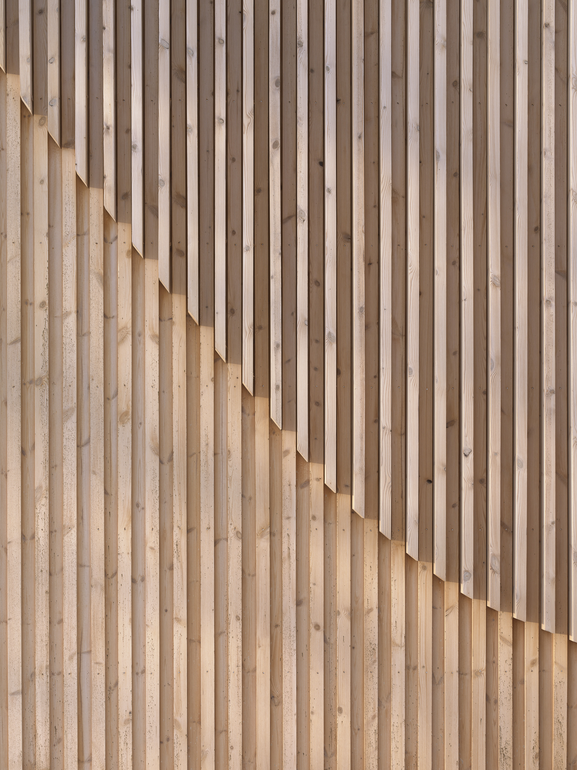 Close-up of staggered timber slat wall creating a rhythmic pattern of light and shadow