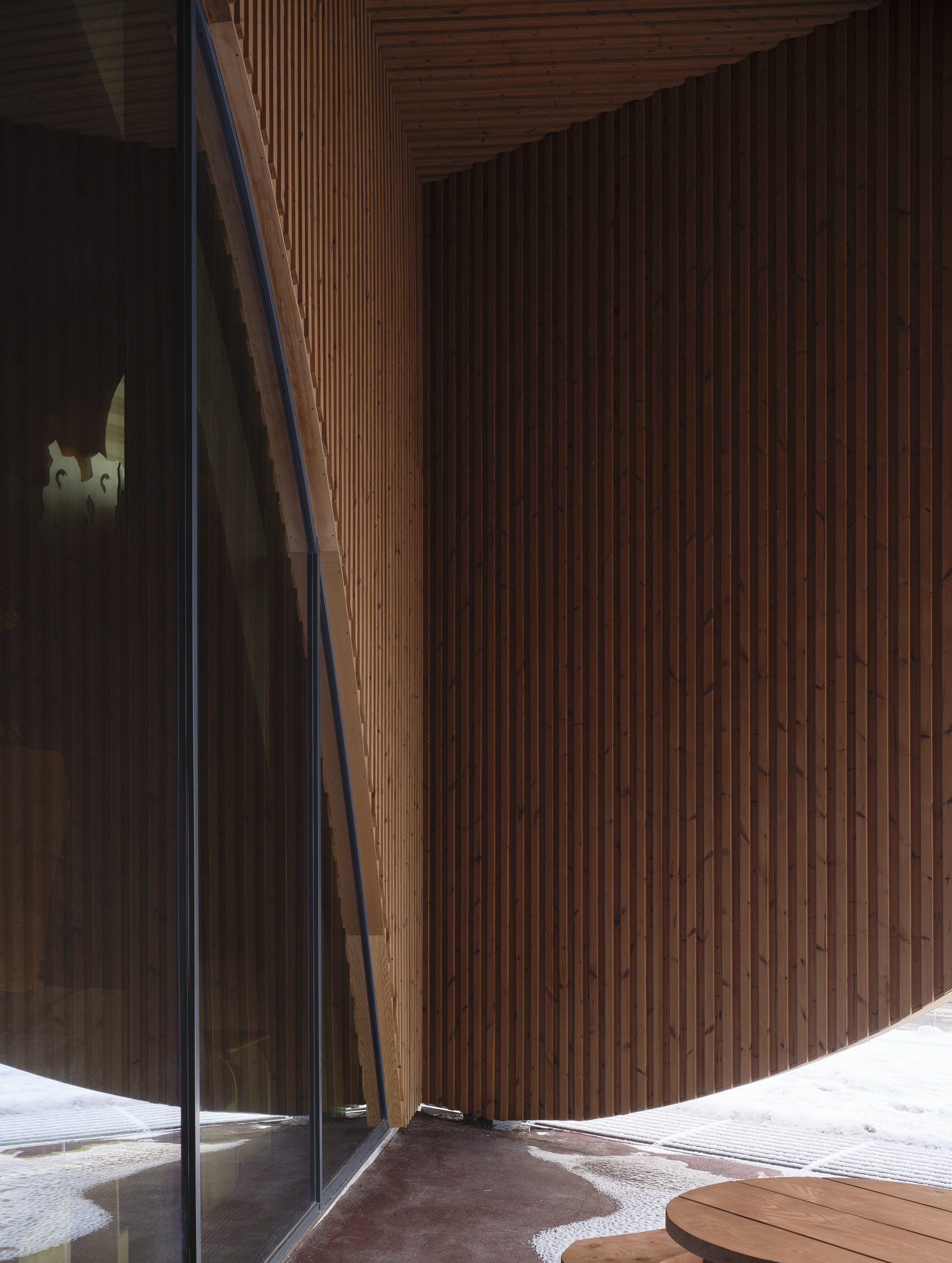 Curved vertical timber slat wall meeting a frameless glass corner at the entrance threshold