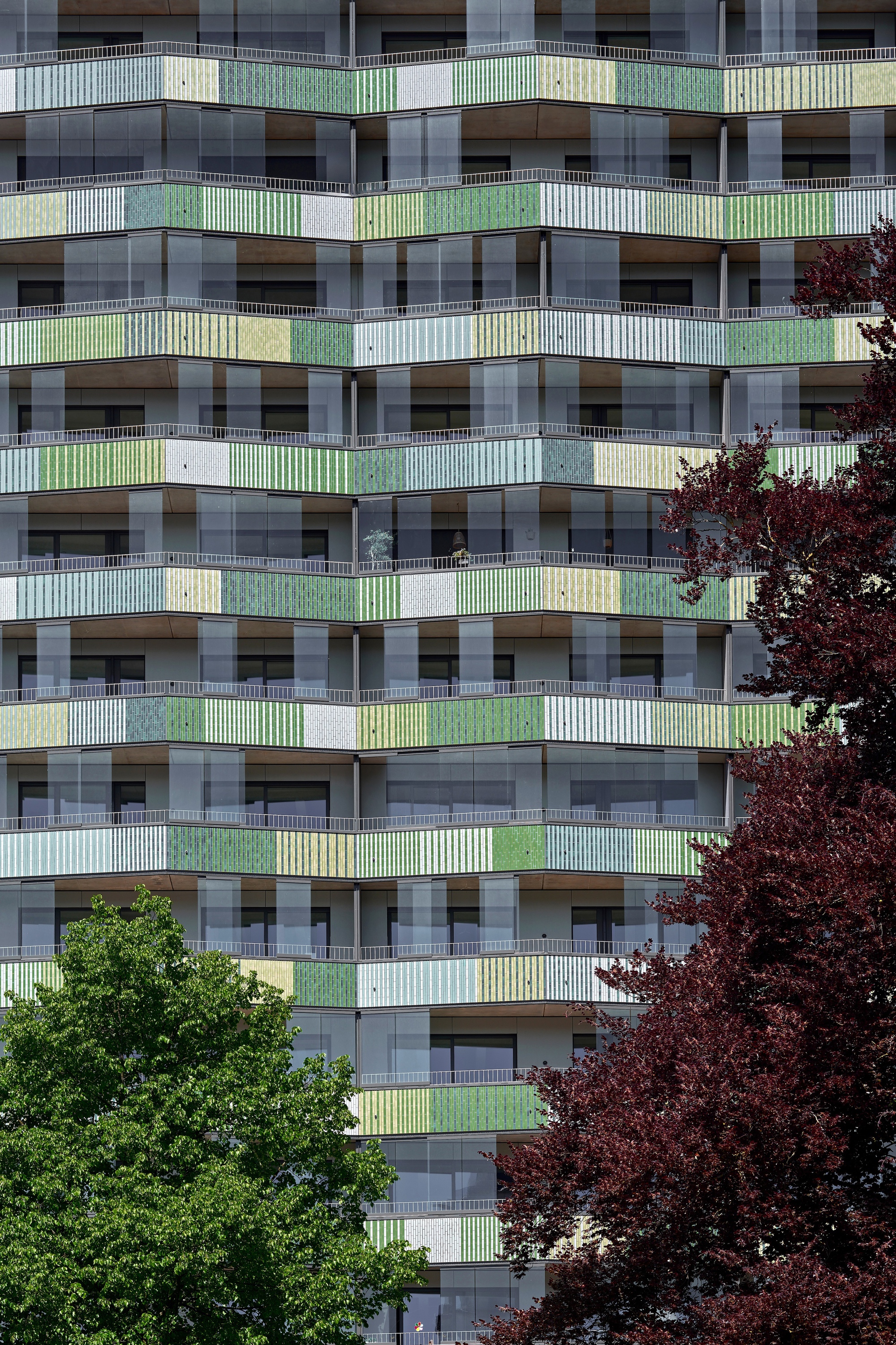 Facade detail showing stacked balconies with green and yellow railings flanked by red and green trees