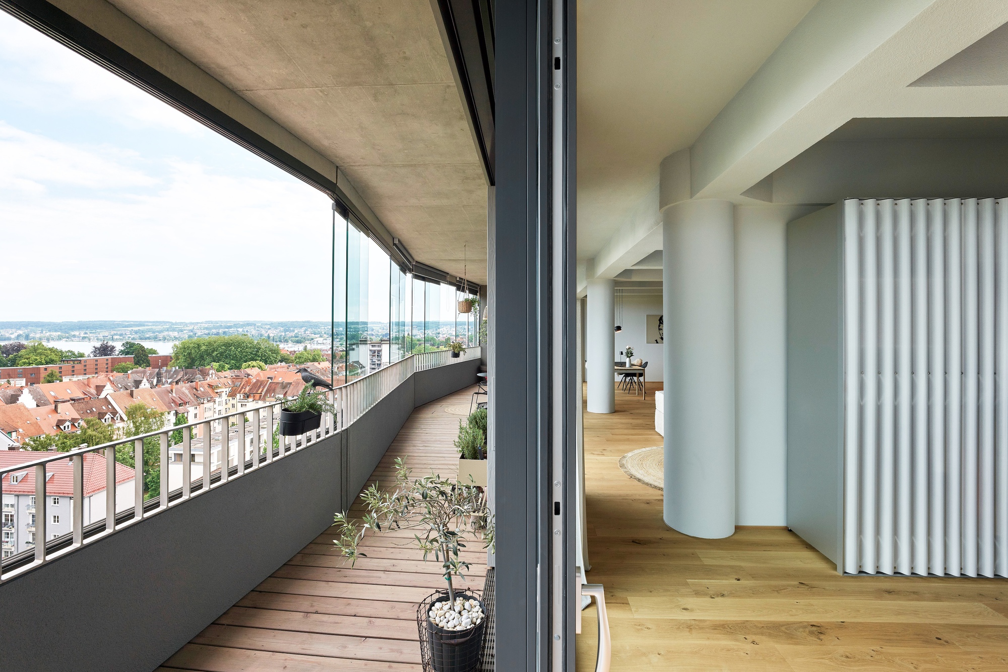 Wooden deck balcony with potted olive tree opening through sliding glass to fluted interior columns