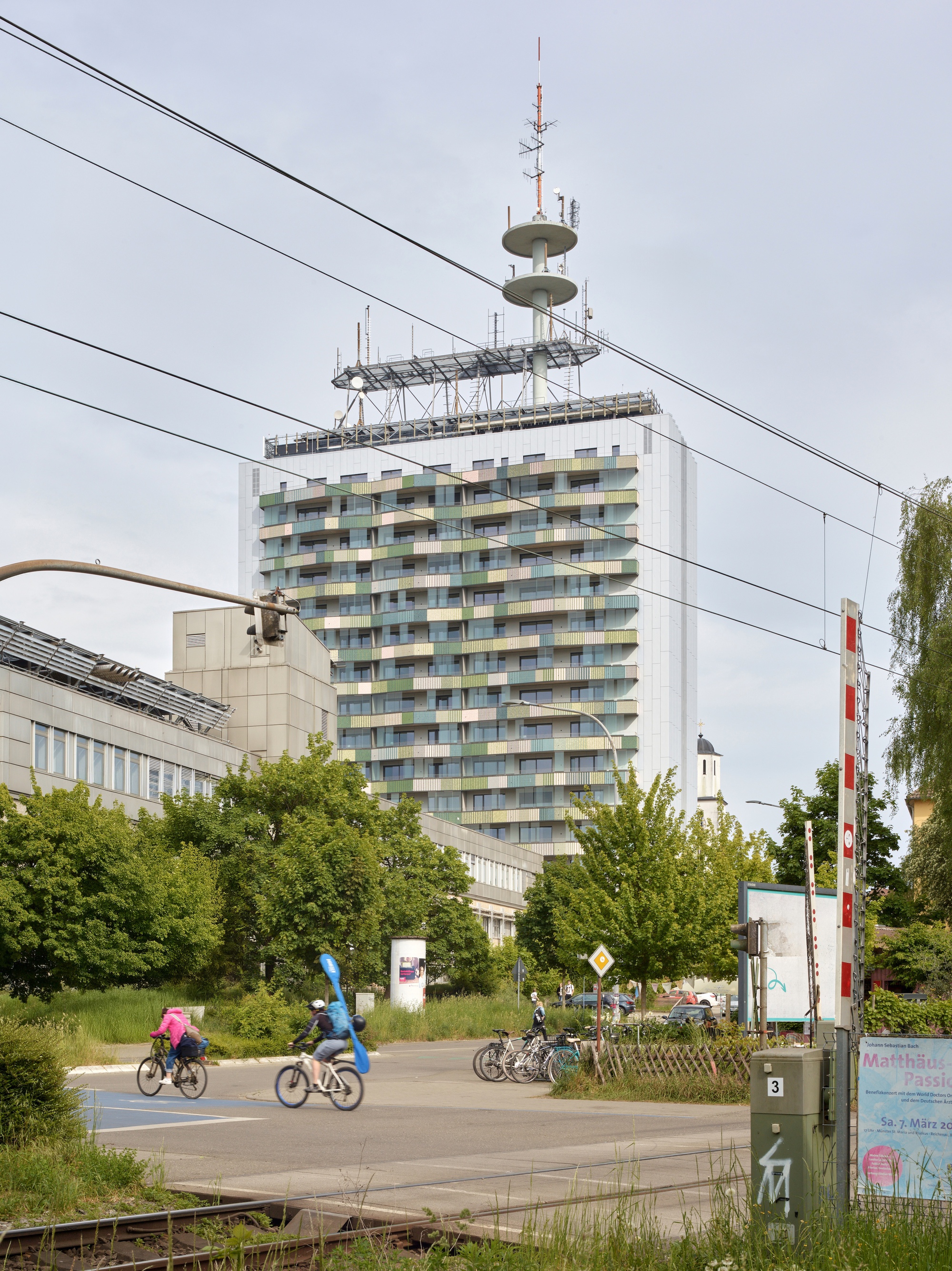 Residential tower with patterned balcony facade viewed from the street with overhead tram cables and cyclists passing