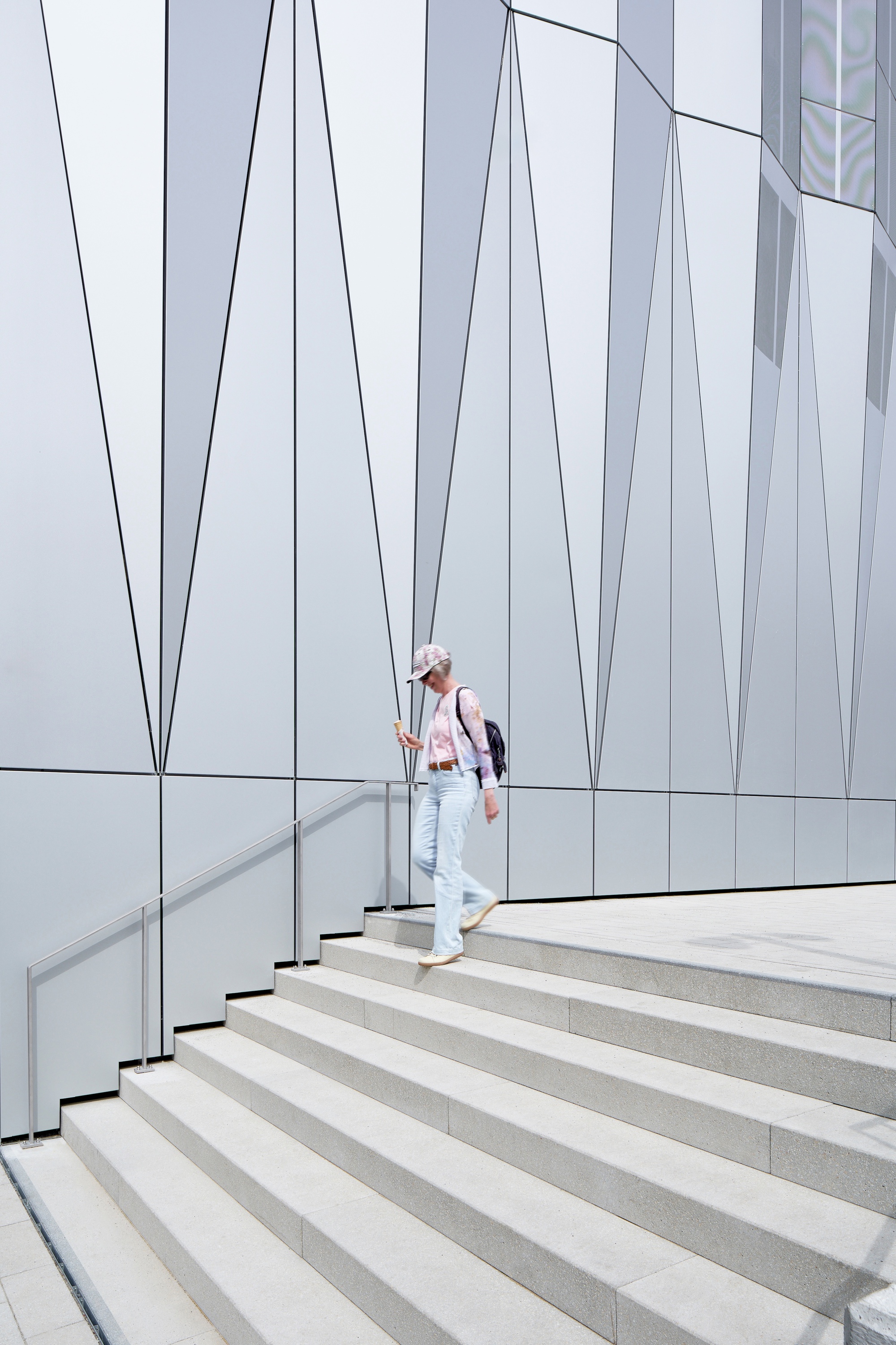 Exterior staircase with metal handrail against a white panel facade with angular black joint lines