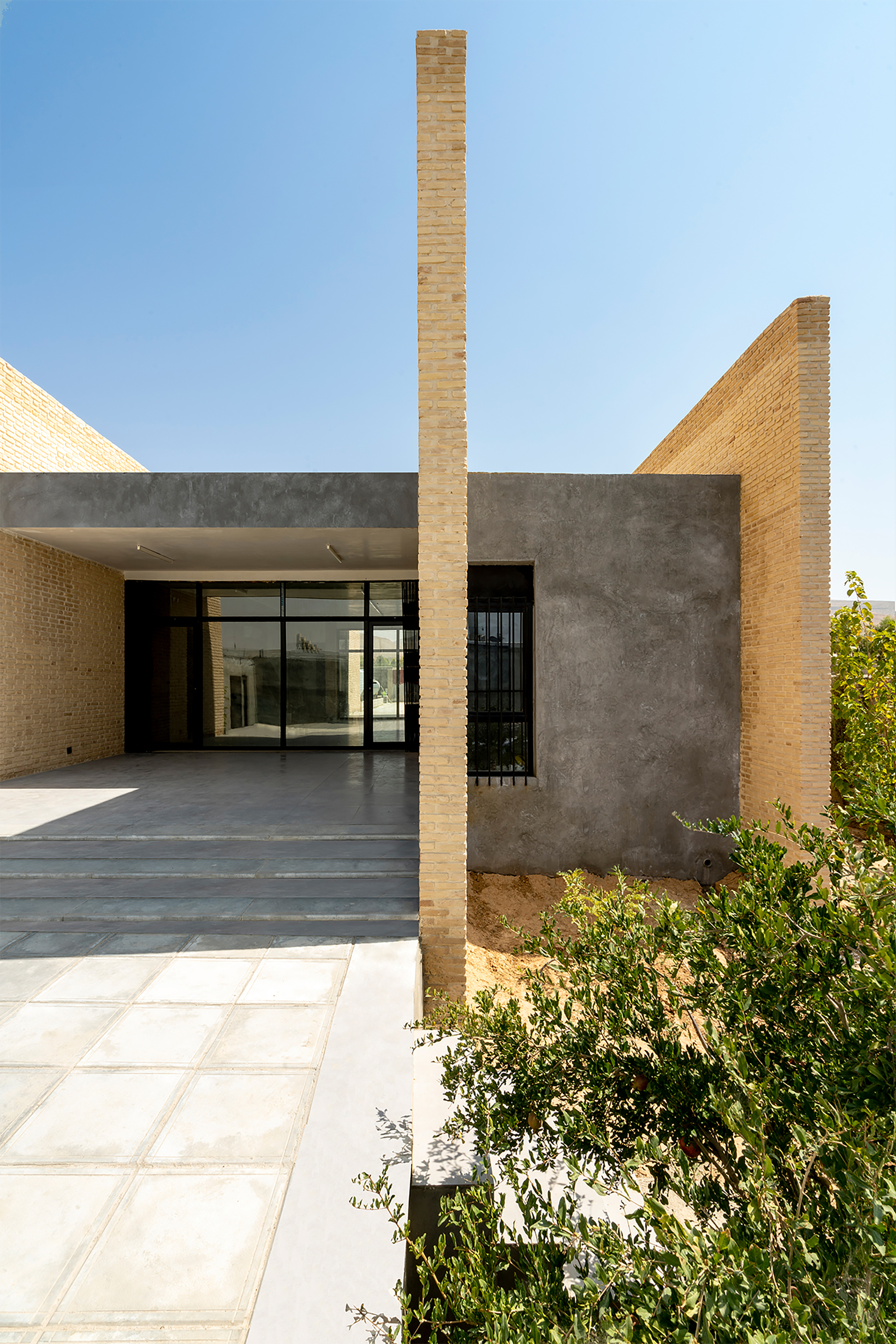 Exterior threshold with slender brick column dividing entrance porch from planted garden bed at edge