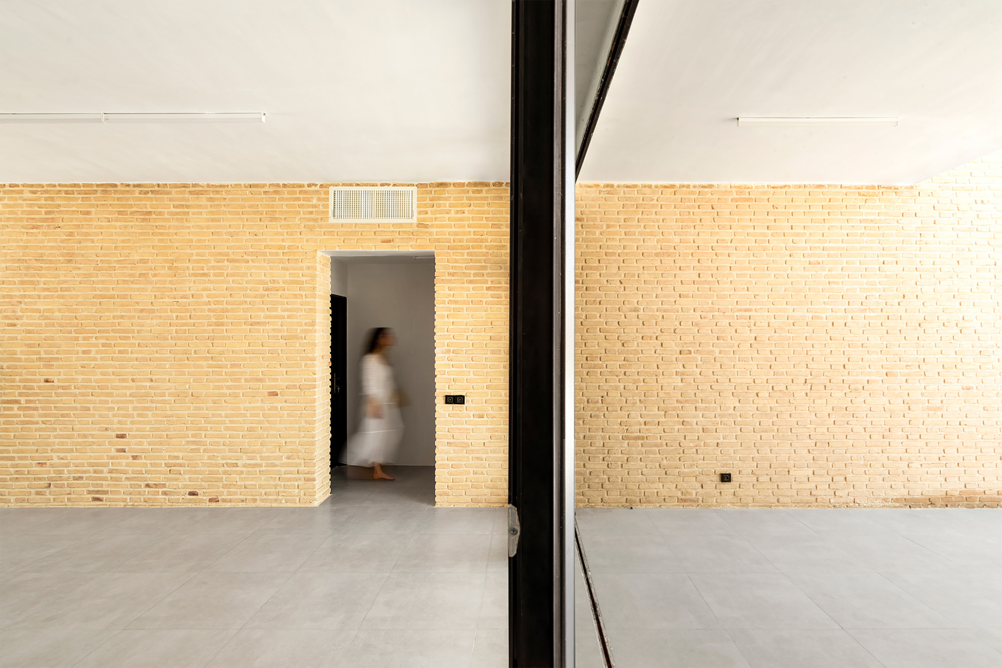 Interior room with pale brick walls and a doorway framing a figure passing through in motion