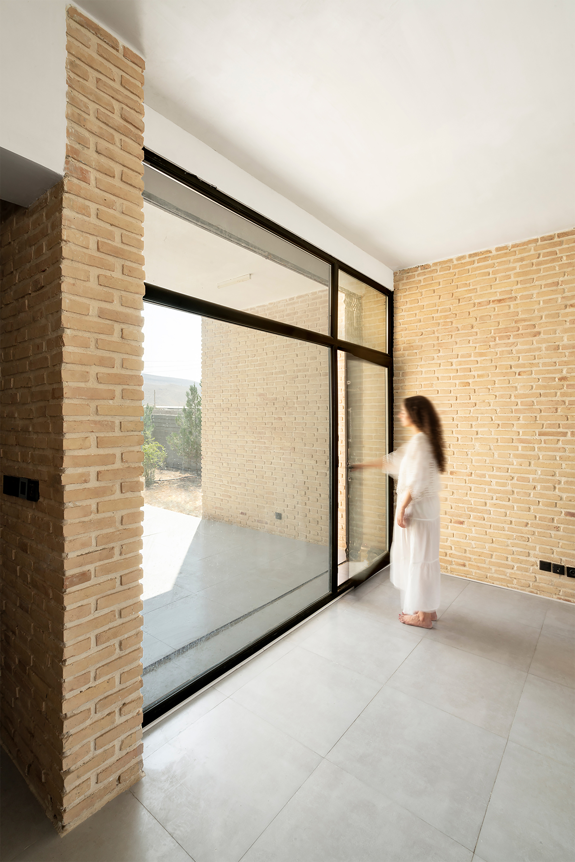 Corner glazed door with black steel frame opening to a brick-walled courtyard as a figure approaches