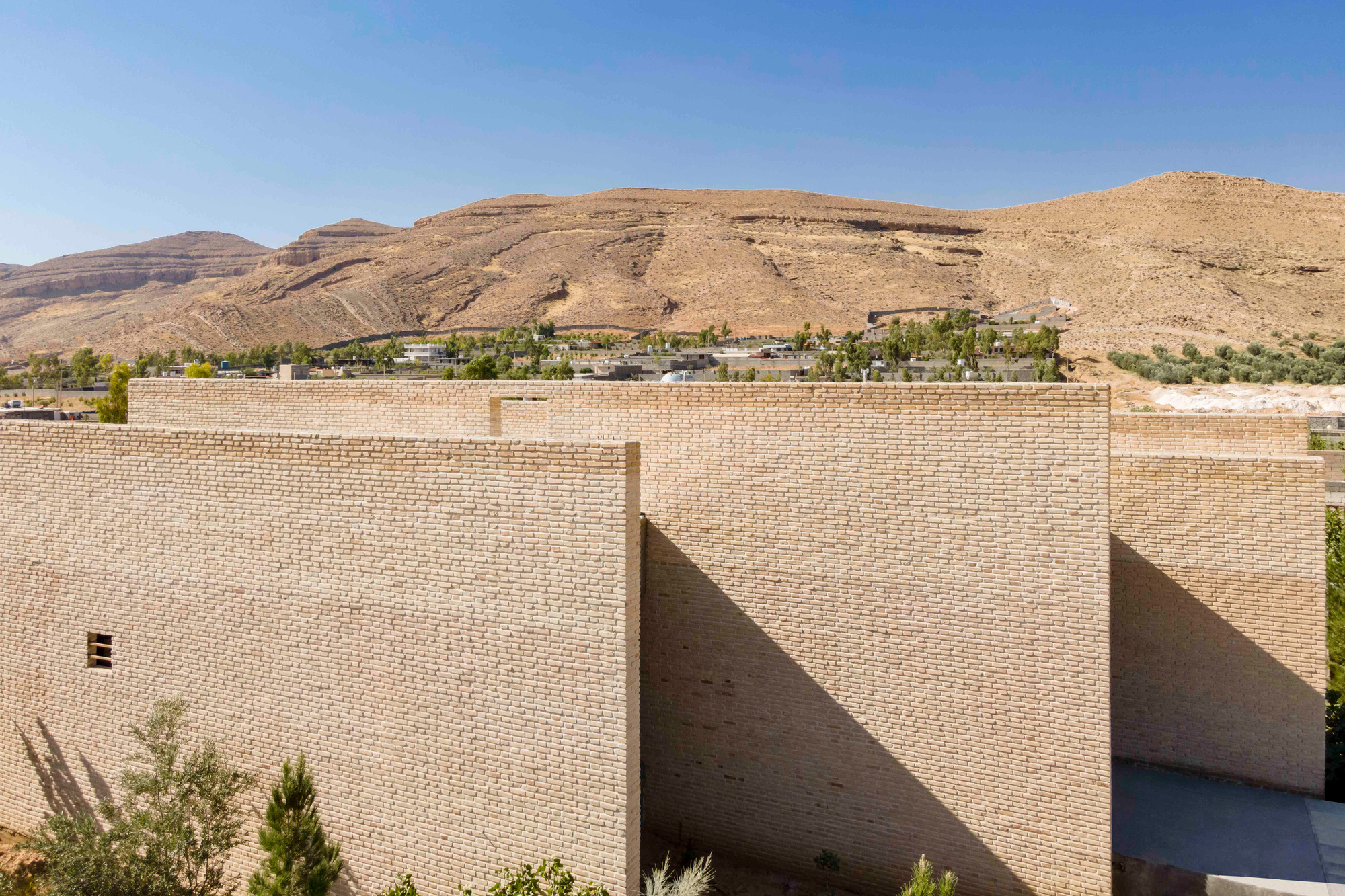 Clustered brick volumes with flat roofs set against a backdrop of barren rolling hills