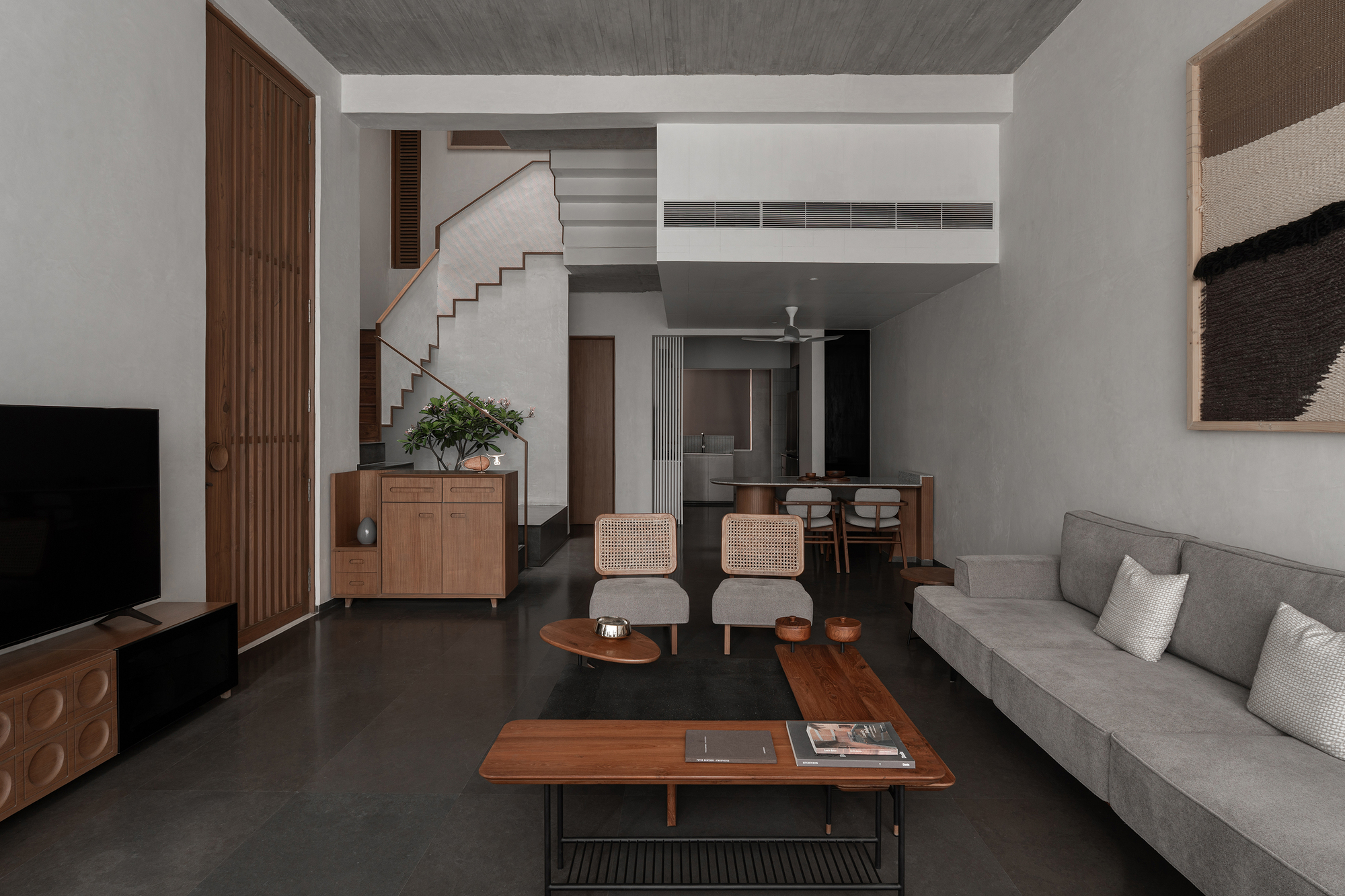 Double-height living room with concrete ceiling, central staircase and polished dark floor