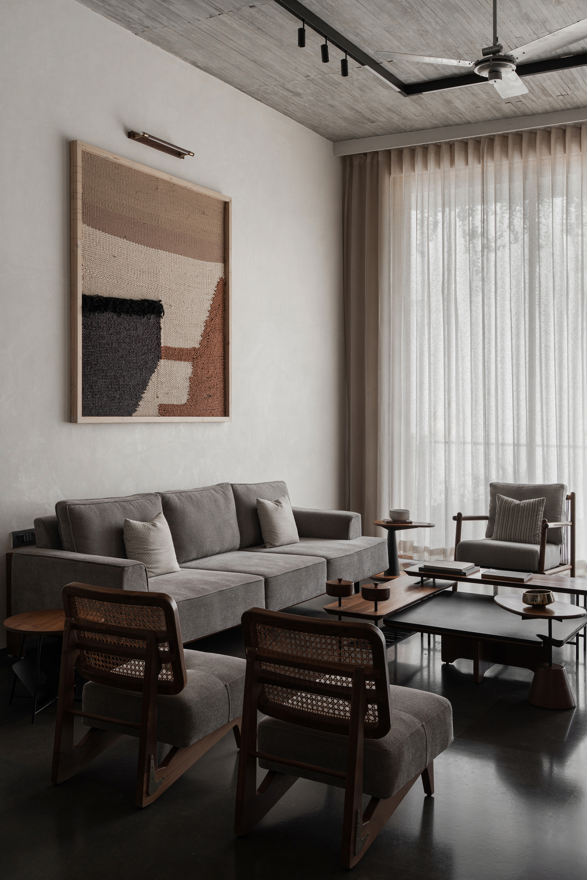 Living area with cane-back chairs, textured wall hanging and sheer curtains filtering daylight