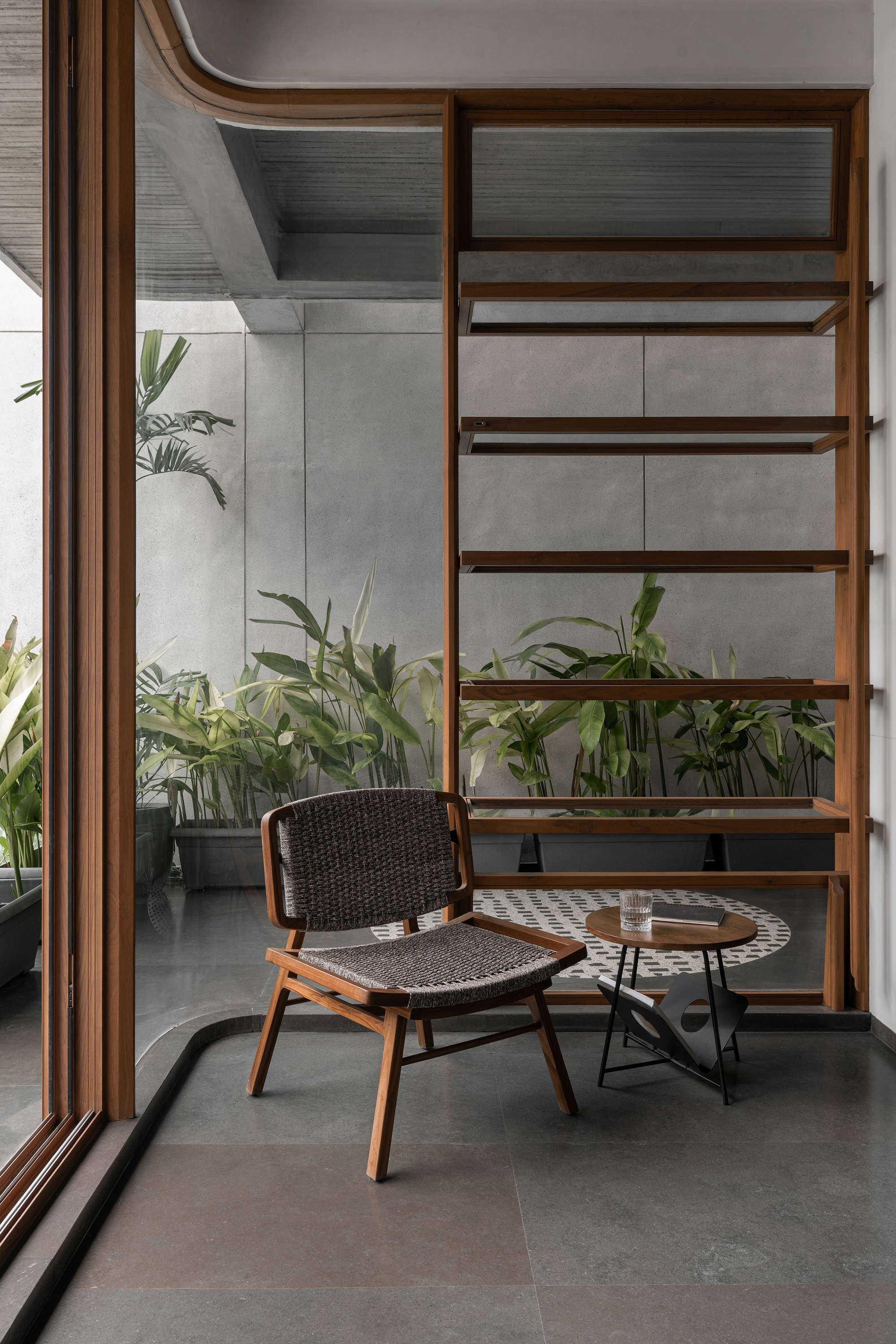 Timber shelving unit beside glazed corner with potted palms in an interior courtyard