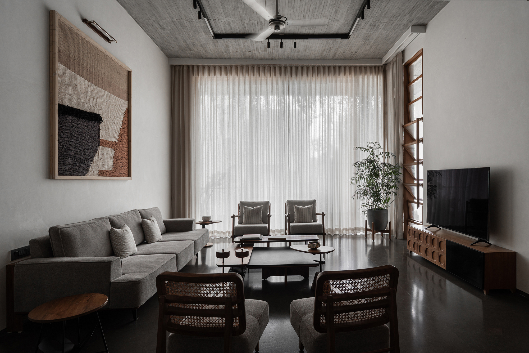 Living room with grey upholstered furniture, cane-backed chairs and sheer curtains filtering daylight