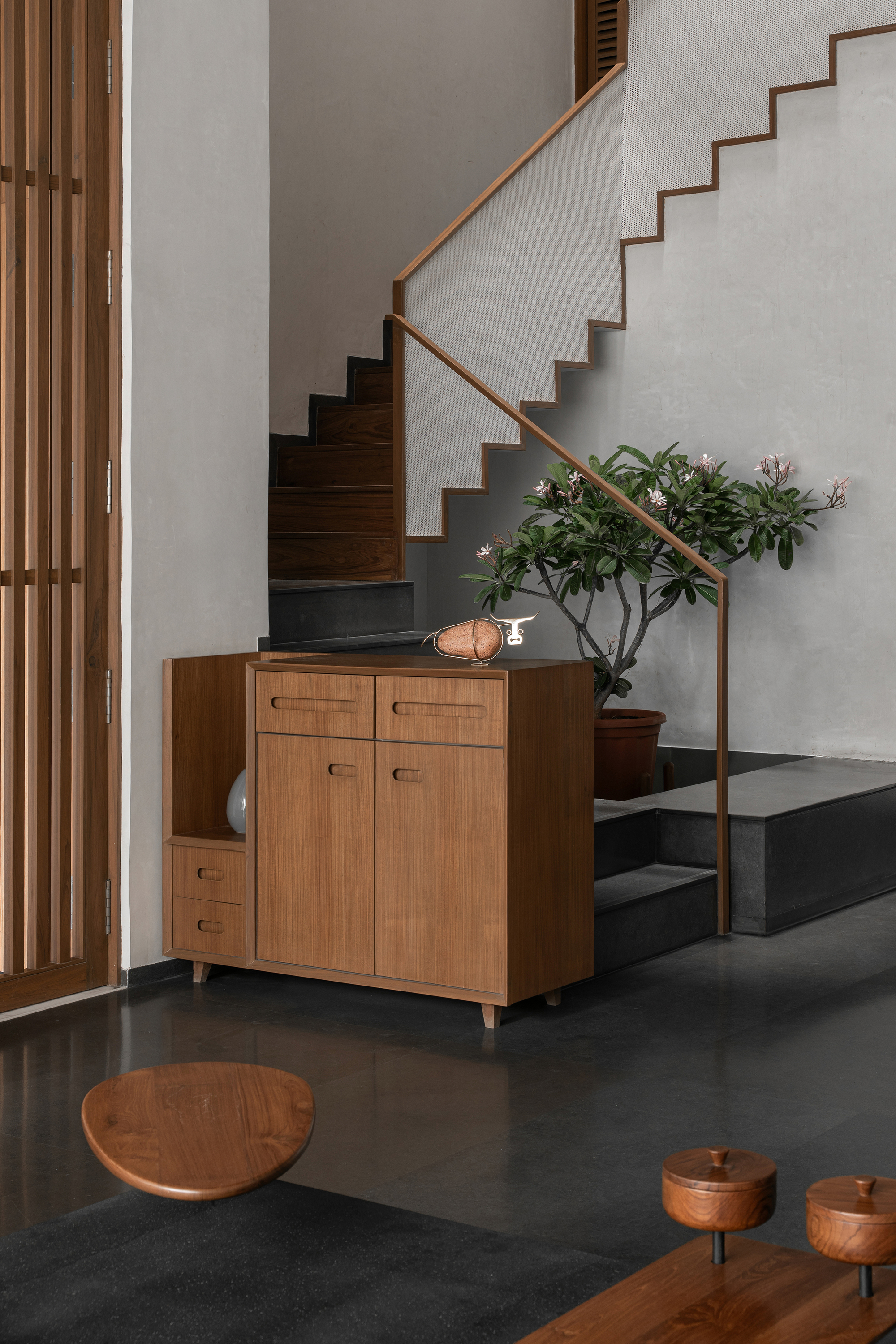 Staircase with dark grey steps, timber railing and mid-century credenza beneath a potted plant