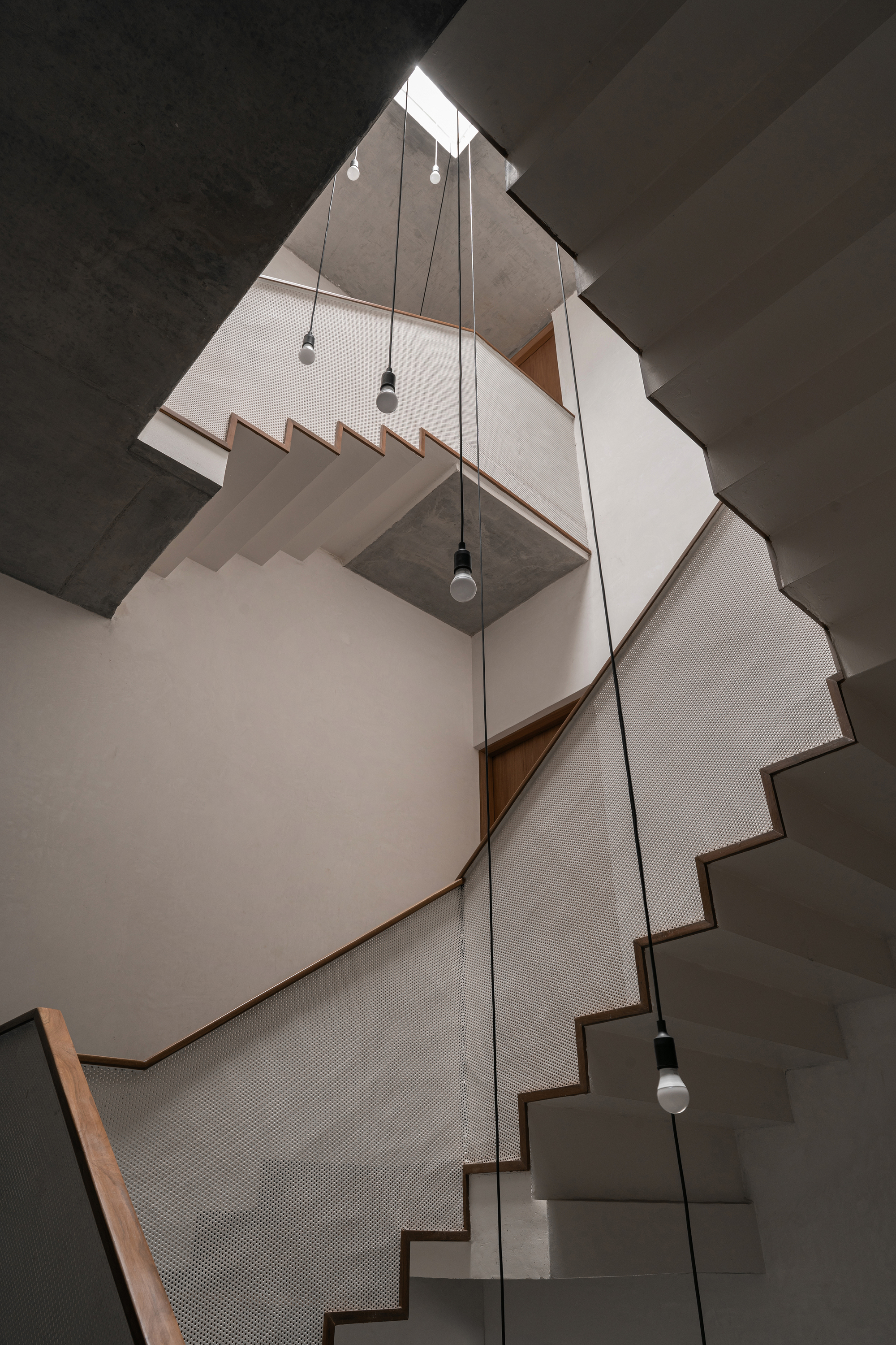 Upward view of multi-level stairwell with pendant lights hanging through the skylit void