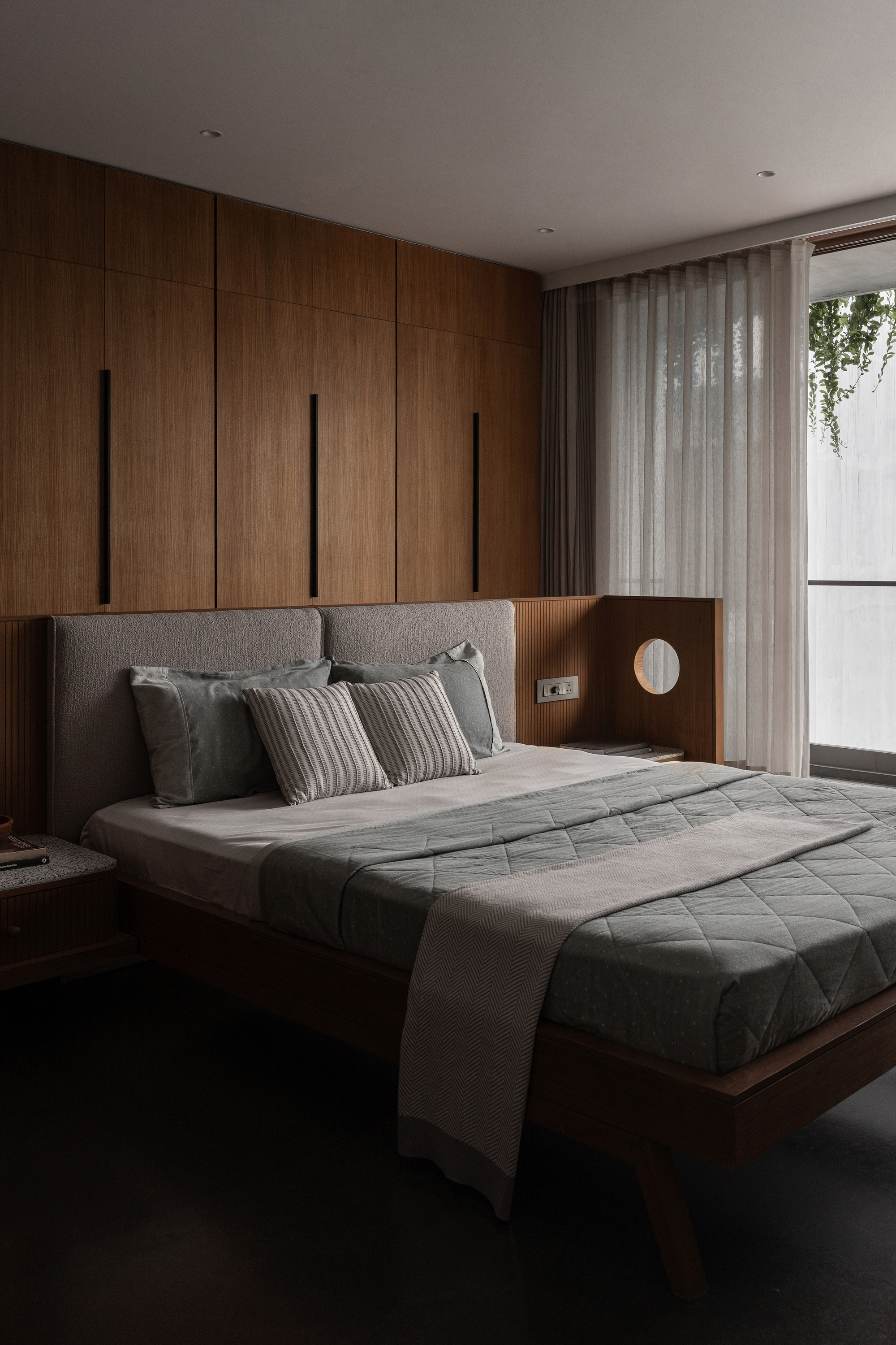 Bedroom with walnut paneled wall storage and integrated bedside niche with circular sconce