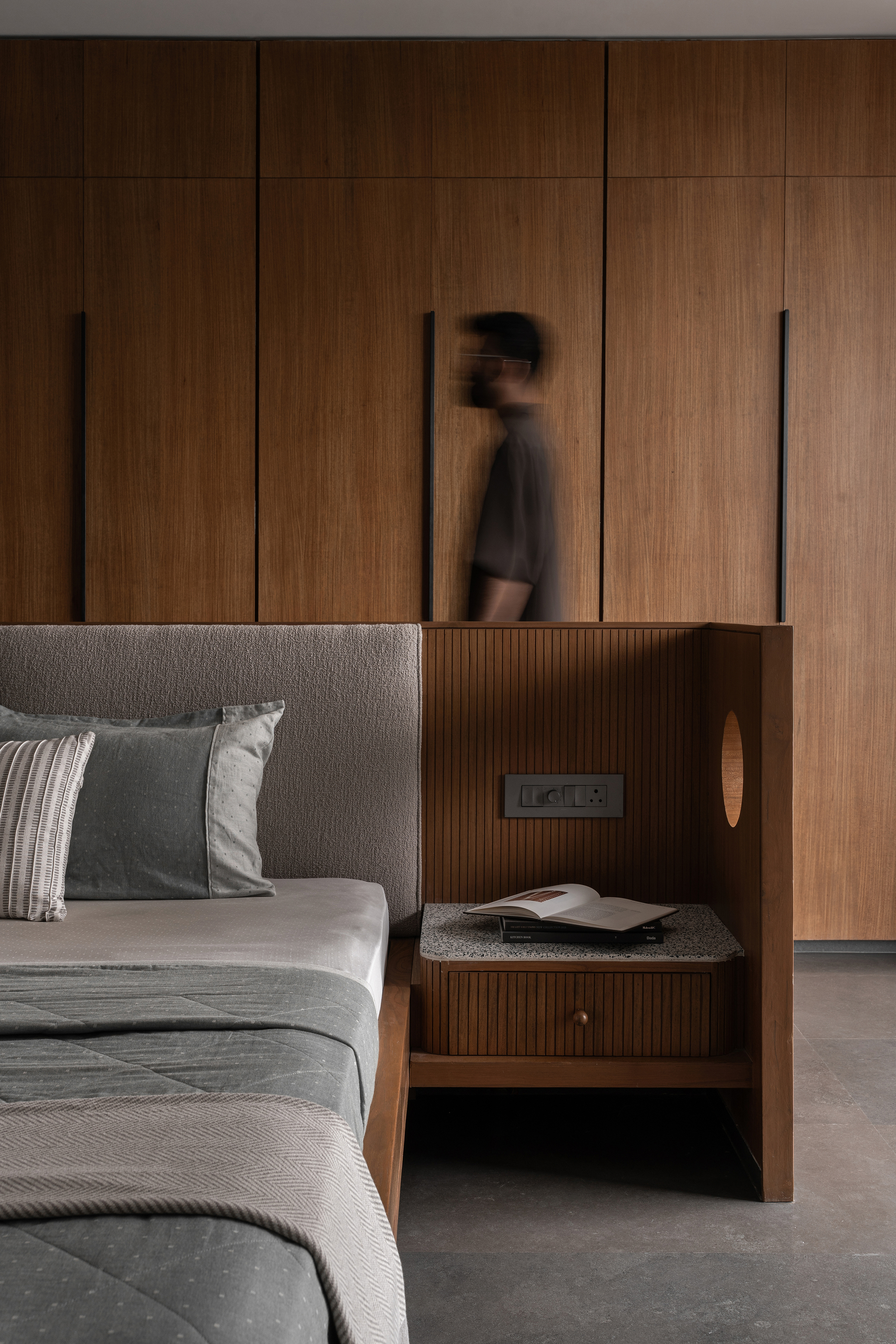 Fluted timber nightstand with stone top and figure passing by the walnut storage wall