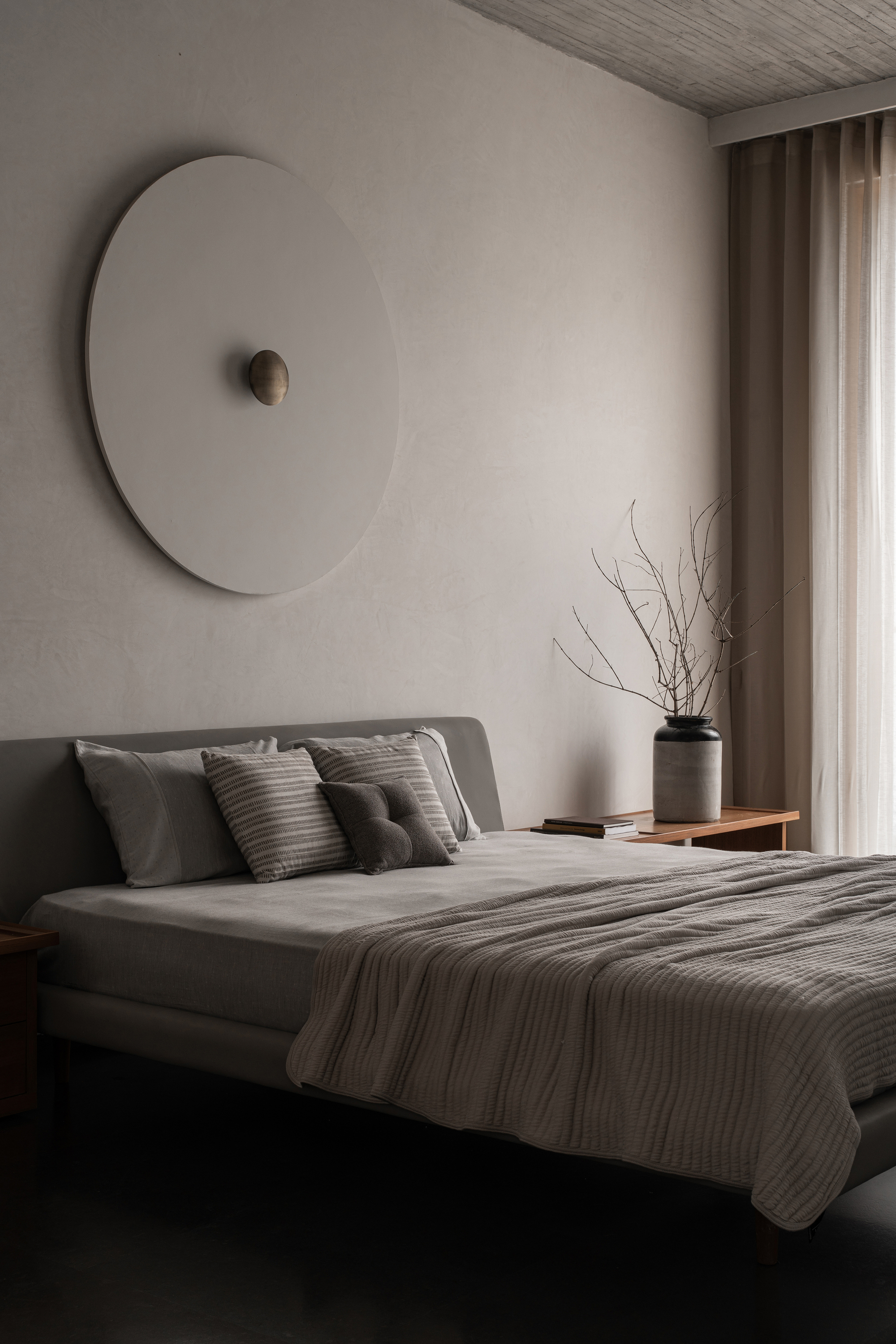 Bedroom wall with circular sculptural element above the bed and branch arrangement on timber shelf