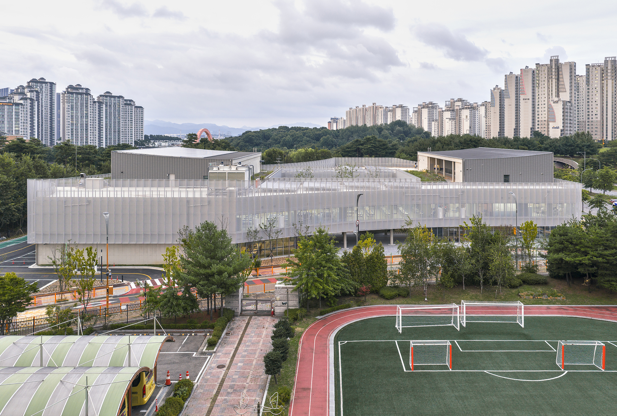 Elevated view of the white perforated metal facade with sports fields and residential towers beyond