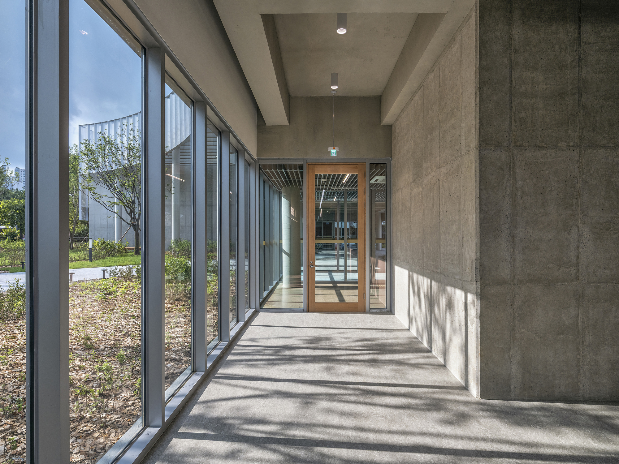 Glazed corridor with exposed concrete ceiling and dappled sunlight on the polished floor