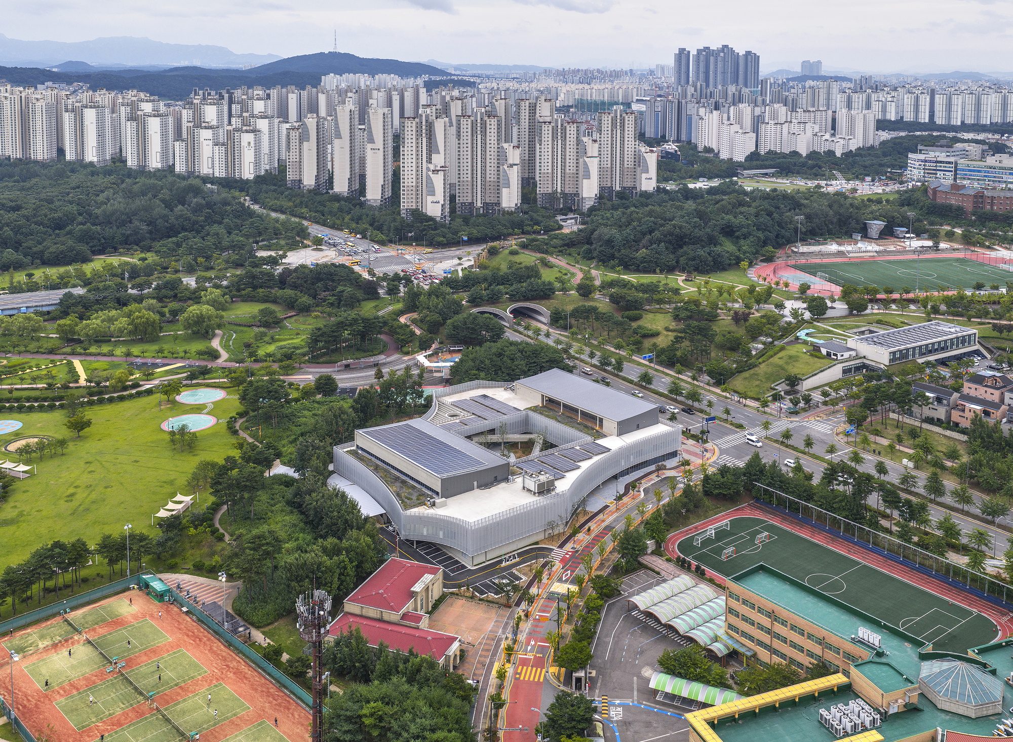 Aerial view of the white complex nestled between parkland tennis courts and surrounding tower blocks