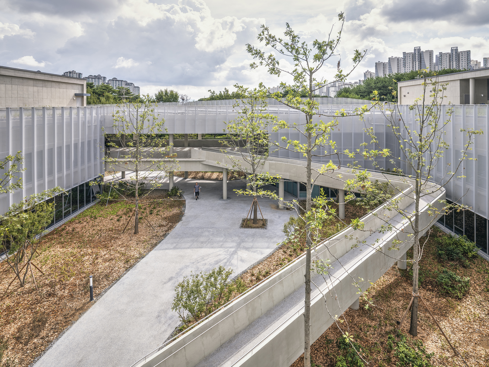 Aerial view of the curved pathway weaving through landscaped berms with young trees under a cloudy sky