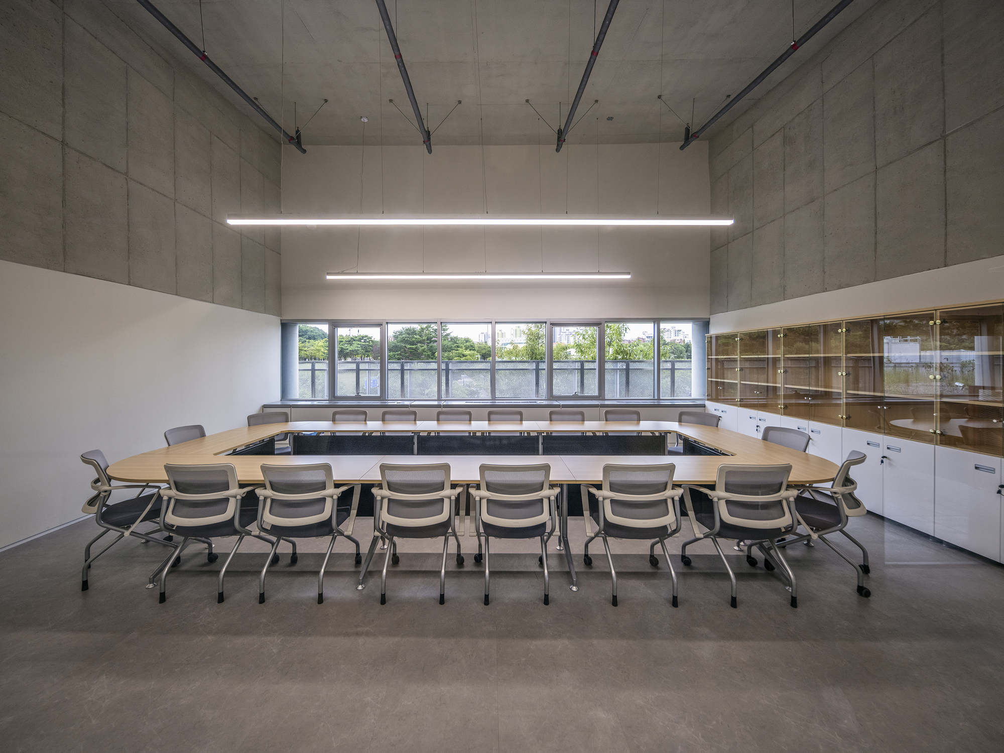 Conference room with U-shaped table arrangement under suspended linear lighting and exposed concrete ceiling
