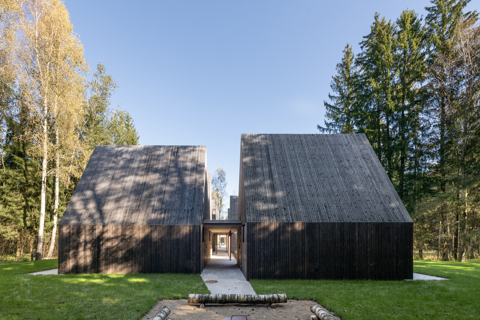 Two gabled volumes clad in dark timber connected by a glazed passage in a forest clearing