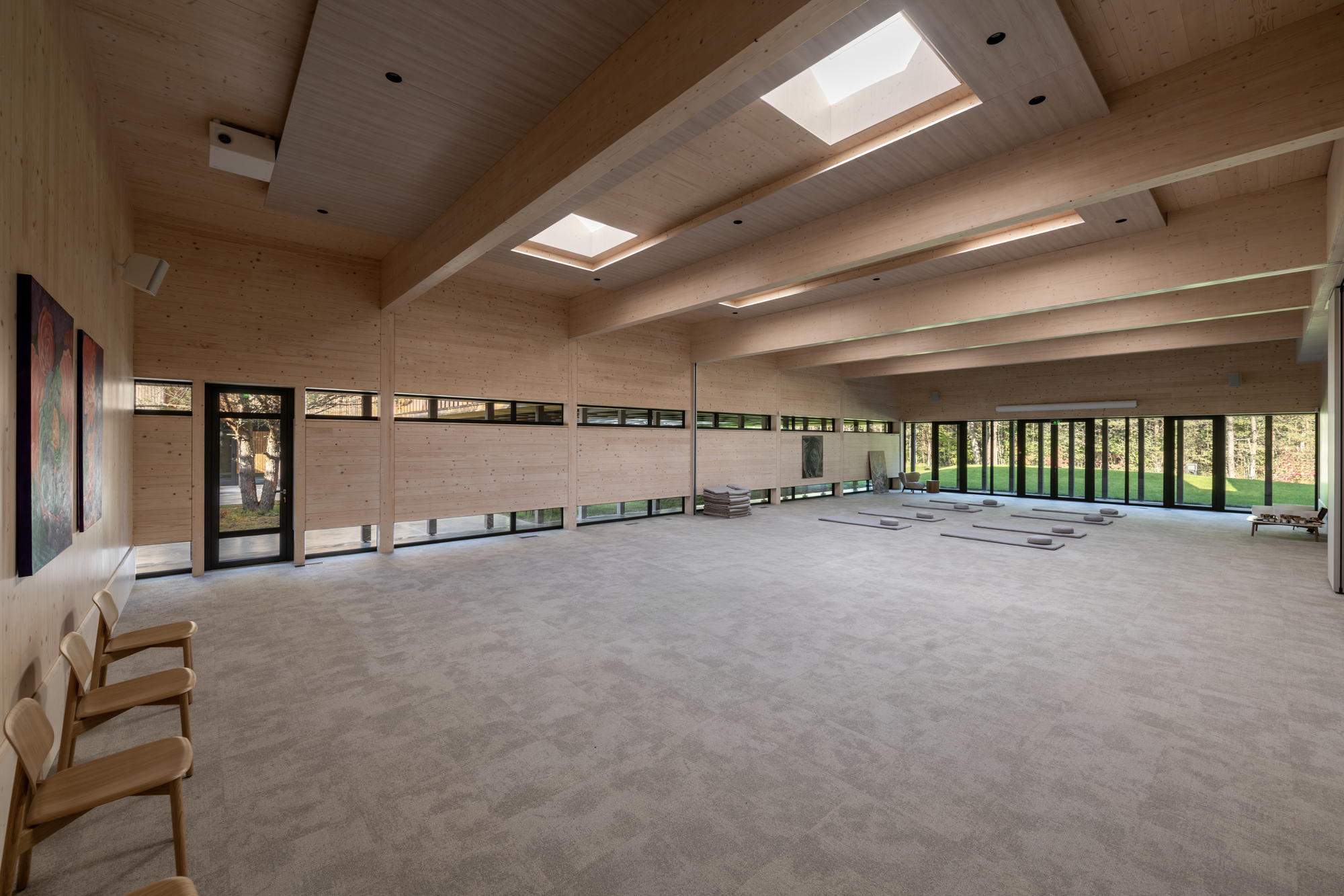 Open interior hall with exposed timber beams, skylights, and ribbon windows overlooking the forest