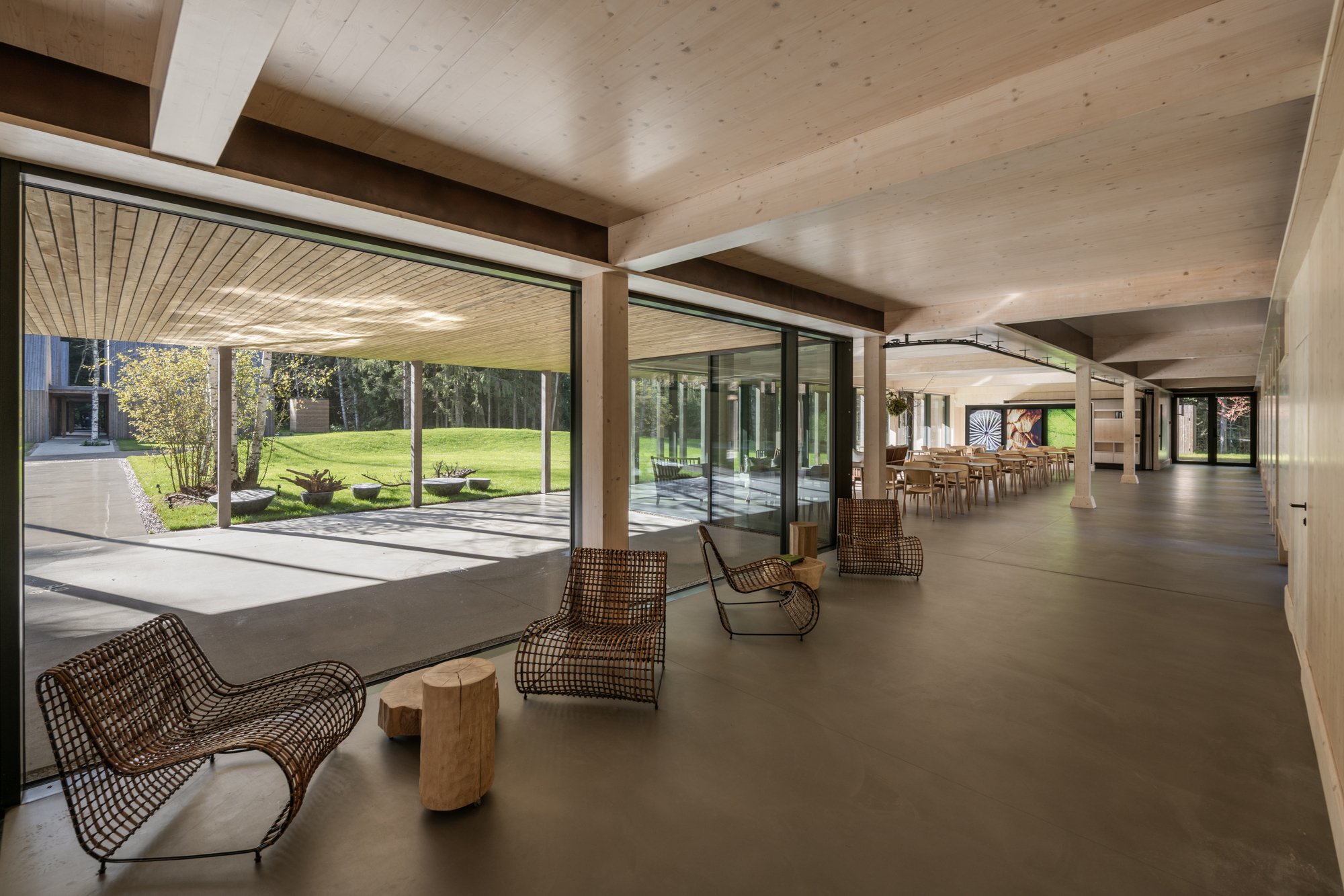 Interior circulation space with rattan lounge chairs opening to a courtyard through floor-to-ceiling glazing
