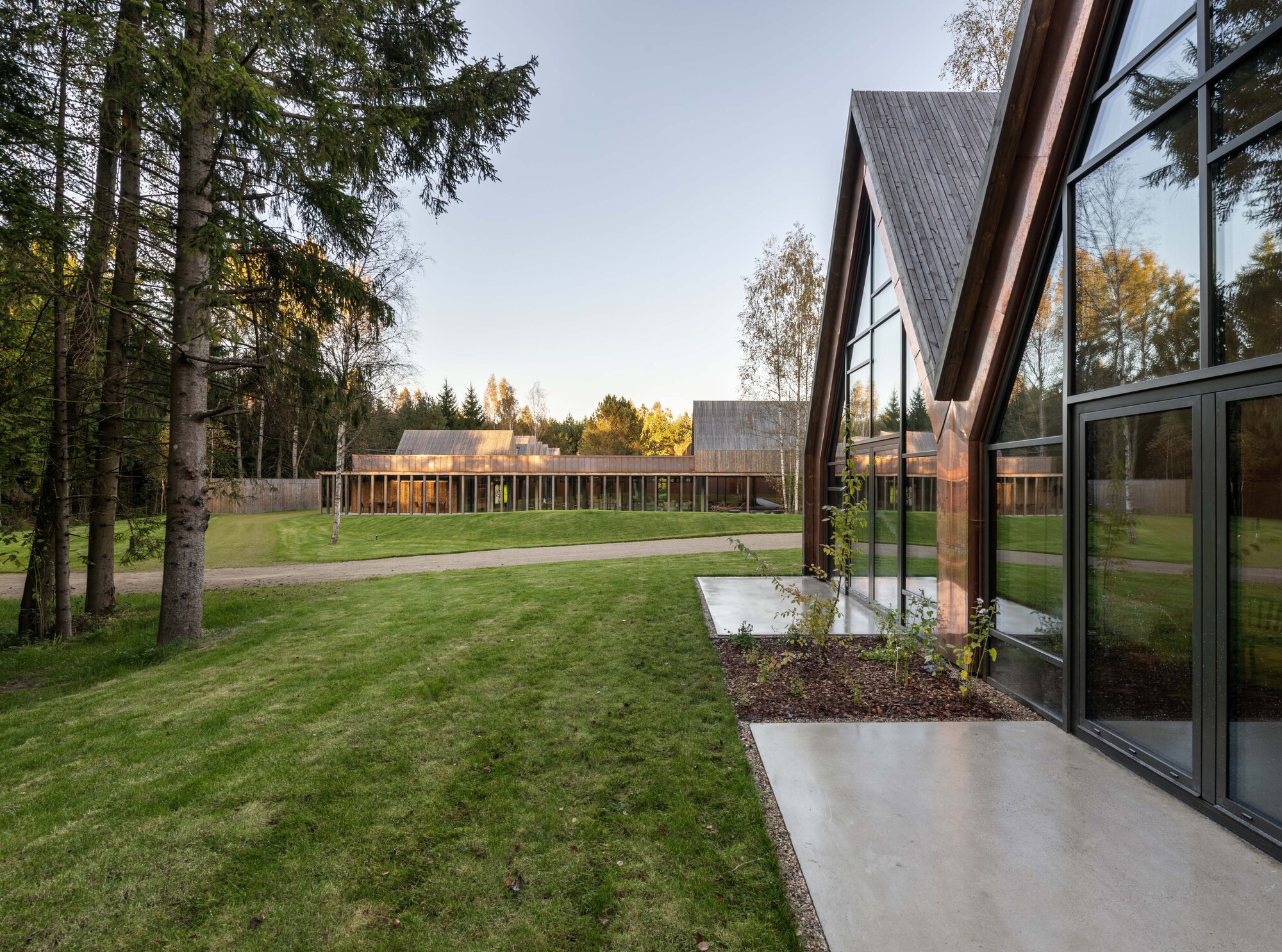 View across the lawn showing linked pavilions with glazed facades and pitched roofs at dusk